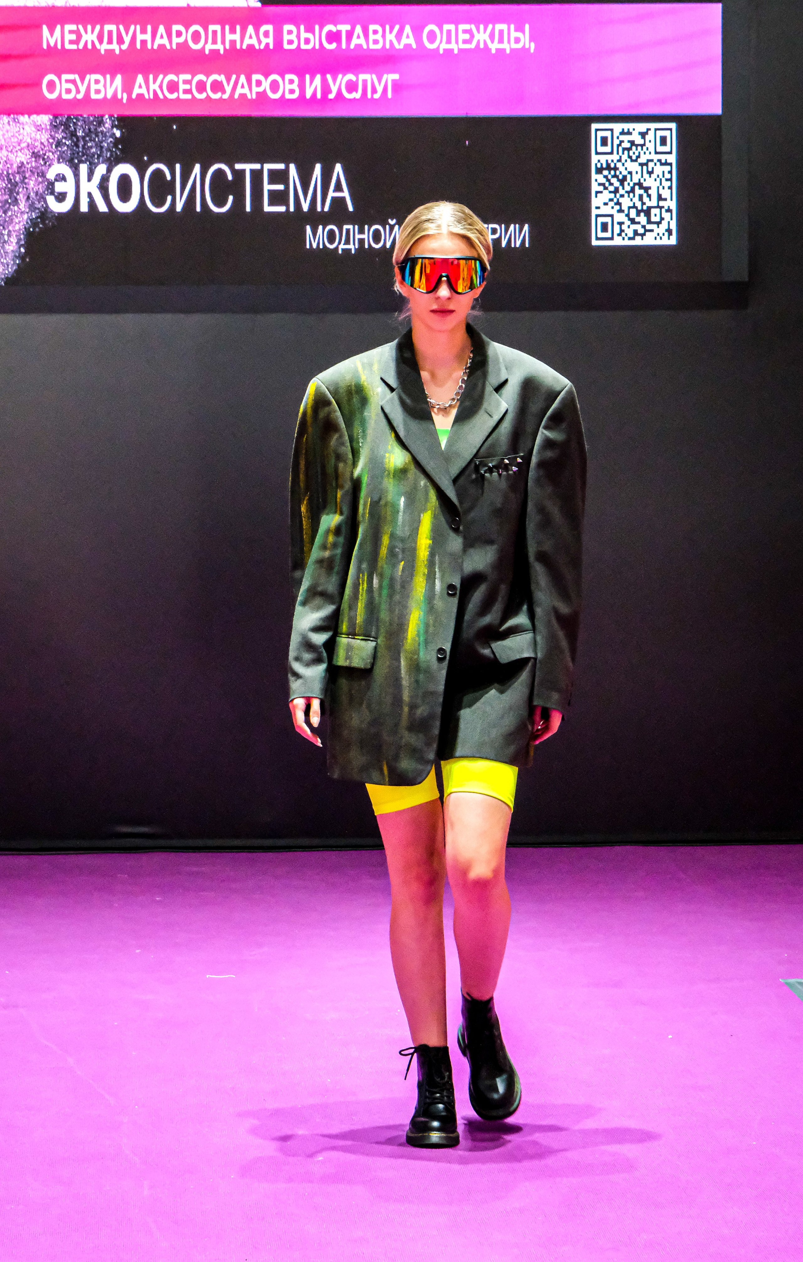  "Модели в ярких нарядах проходят по подиуму во время показа мод, освещенные яркими софитами и окруженные восторженными зрителями."