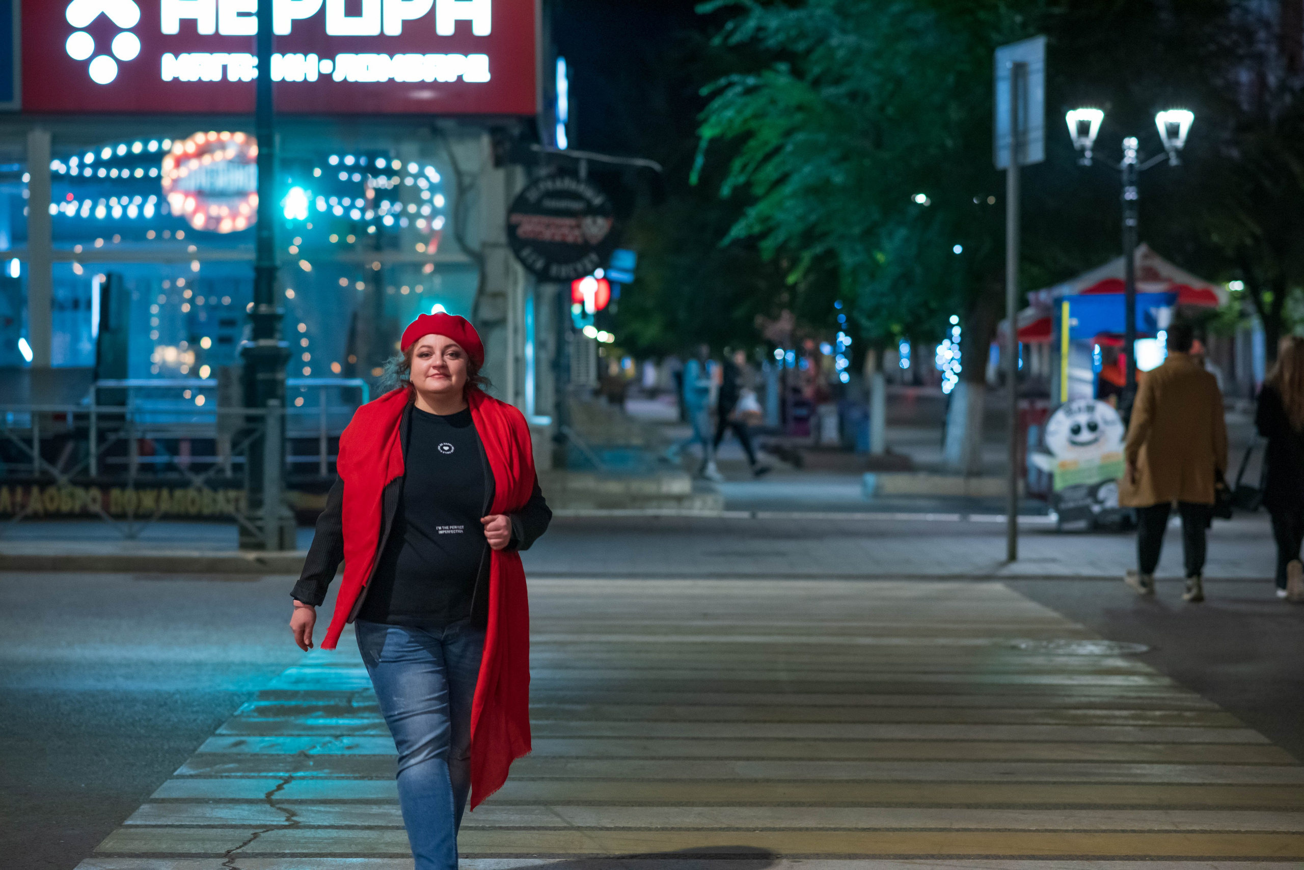 Яркая женщина в красном берете и красном шарфе переходит дорогу по зебре. 