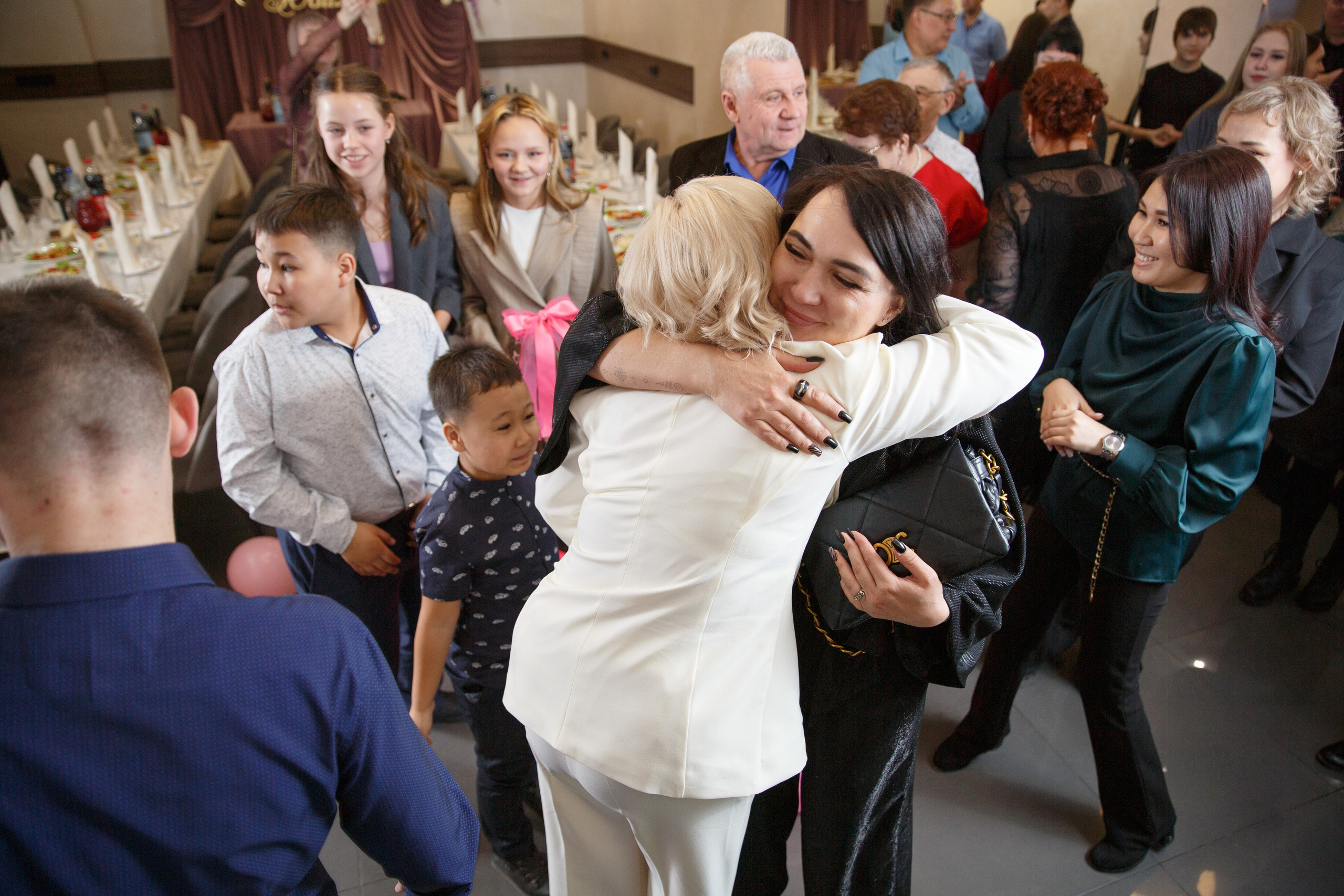 Женщина в белом обнимает гостя, приятные эмоции.