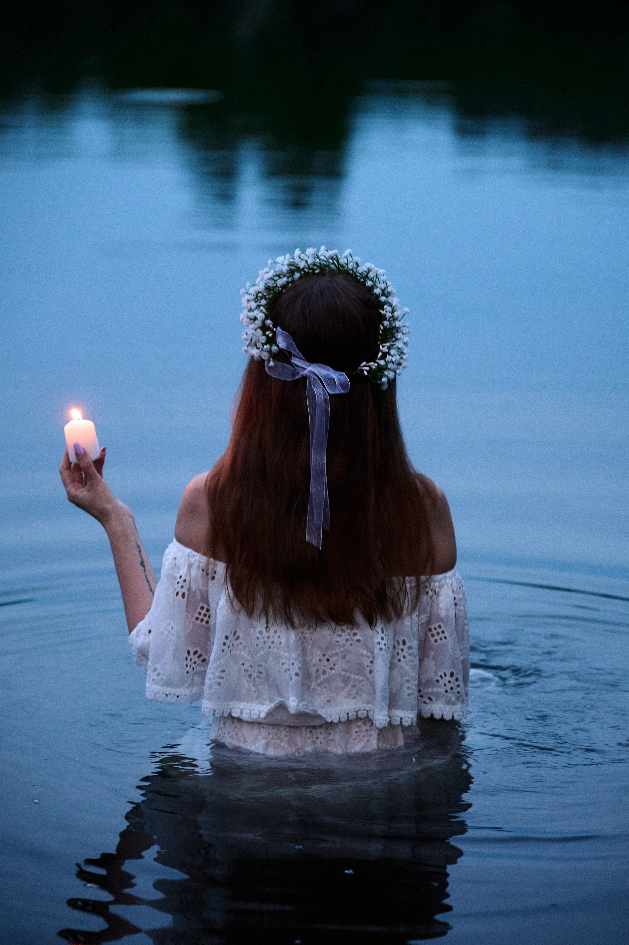 Евгения с венком на голове стоит в озере, держа свечу в руке