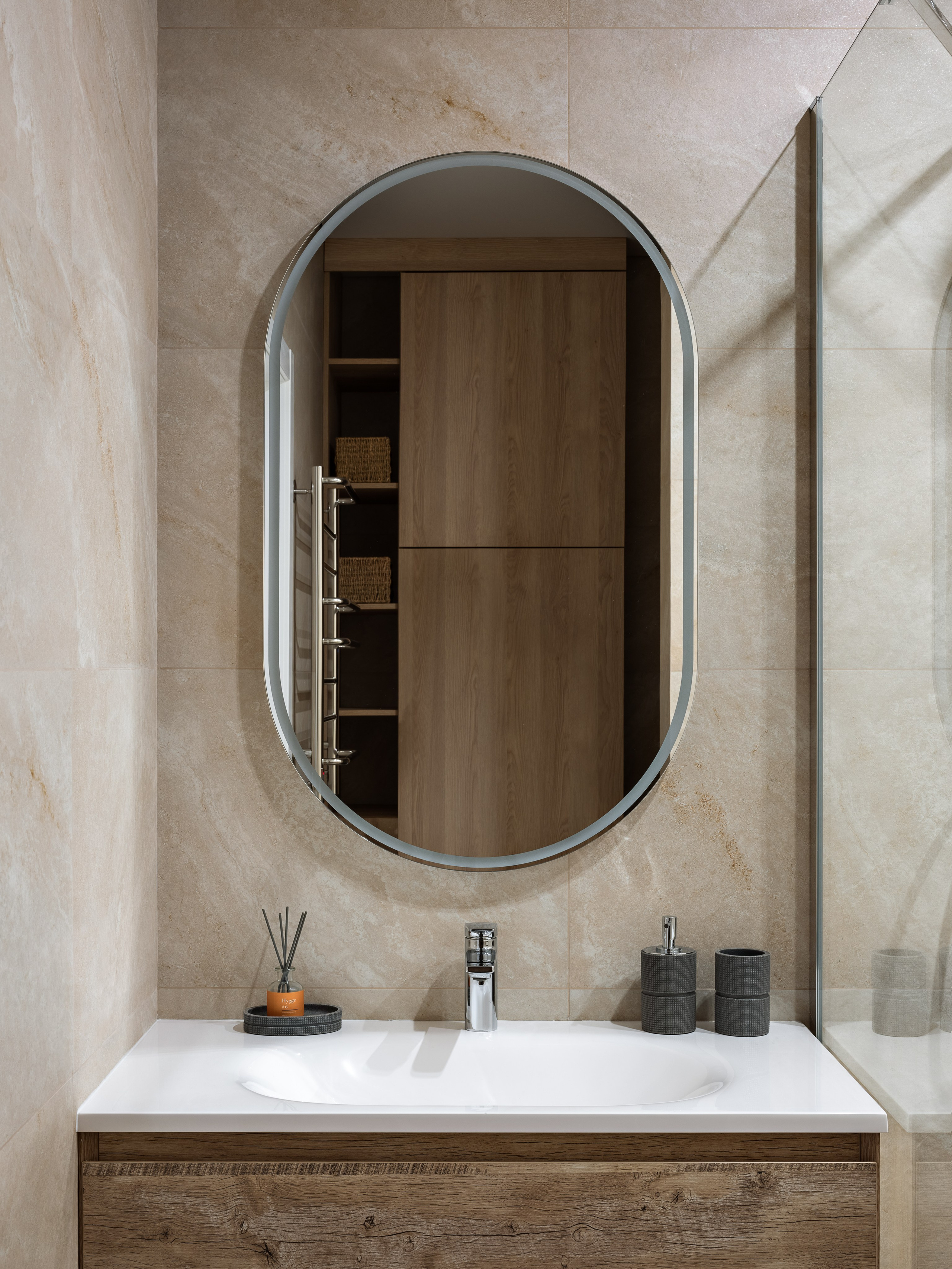 Интерьер ванной комнаты с овальным зеркалом, раковиной и деревянной тумбой, декорированной минималистичными аксессуарами в скандинавском стиле. Дизайн от Натальи Бунеевой, стилист Наталья Якушева, фото Сергей Денисенко.