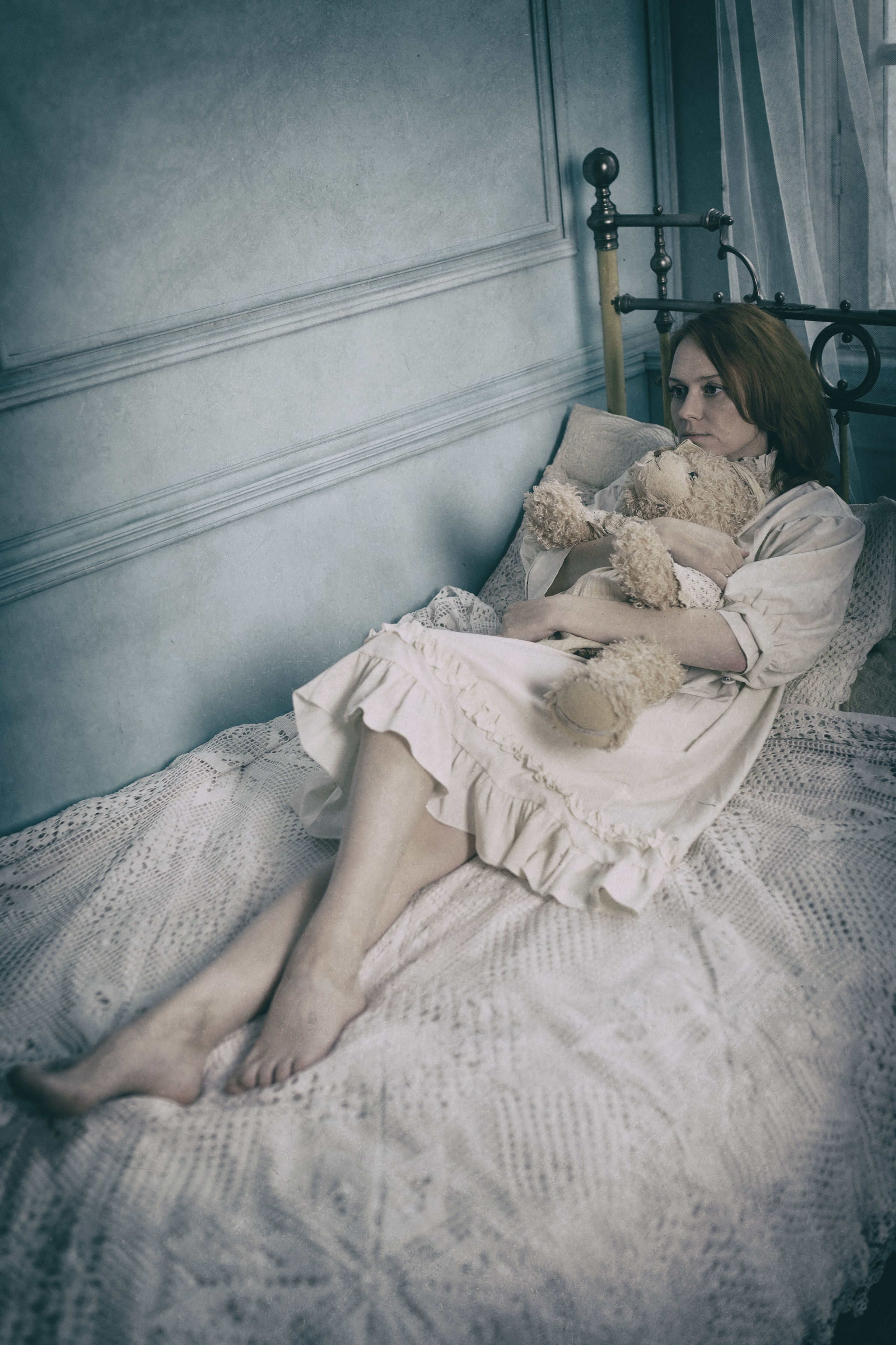 Девушка лежит на кровати, обнимая мягкую игрушки