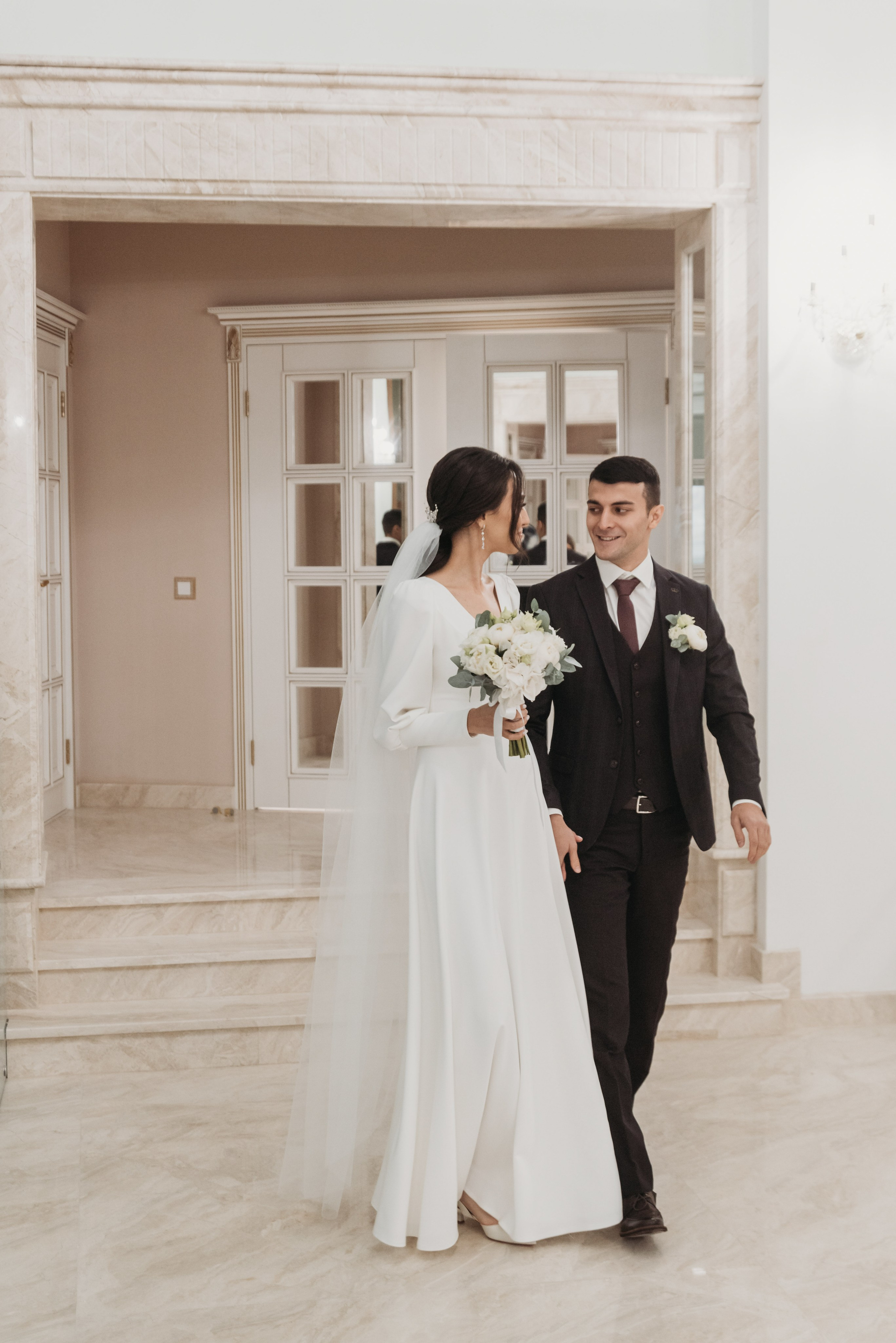 Счастливая пара на свадебной церемонии, входящая в тверской загс. Невеста в элегантном белом платье с букетом, жених в классическом костюме. Идеальный момент для свадебной фотографии, запечатлевающий радость и любовь в важный день