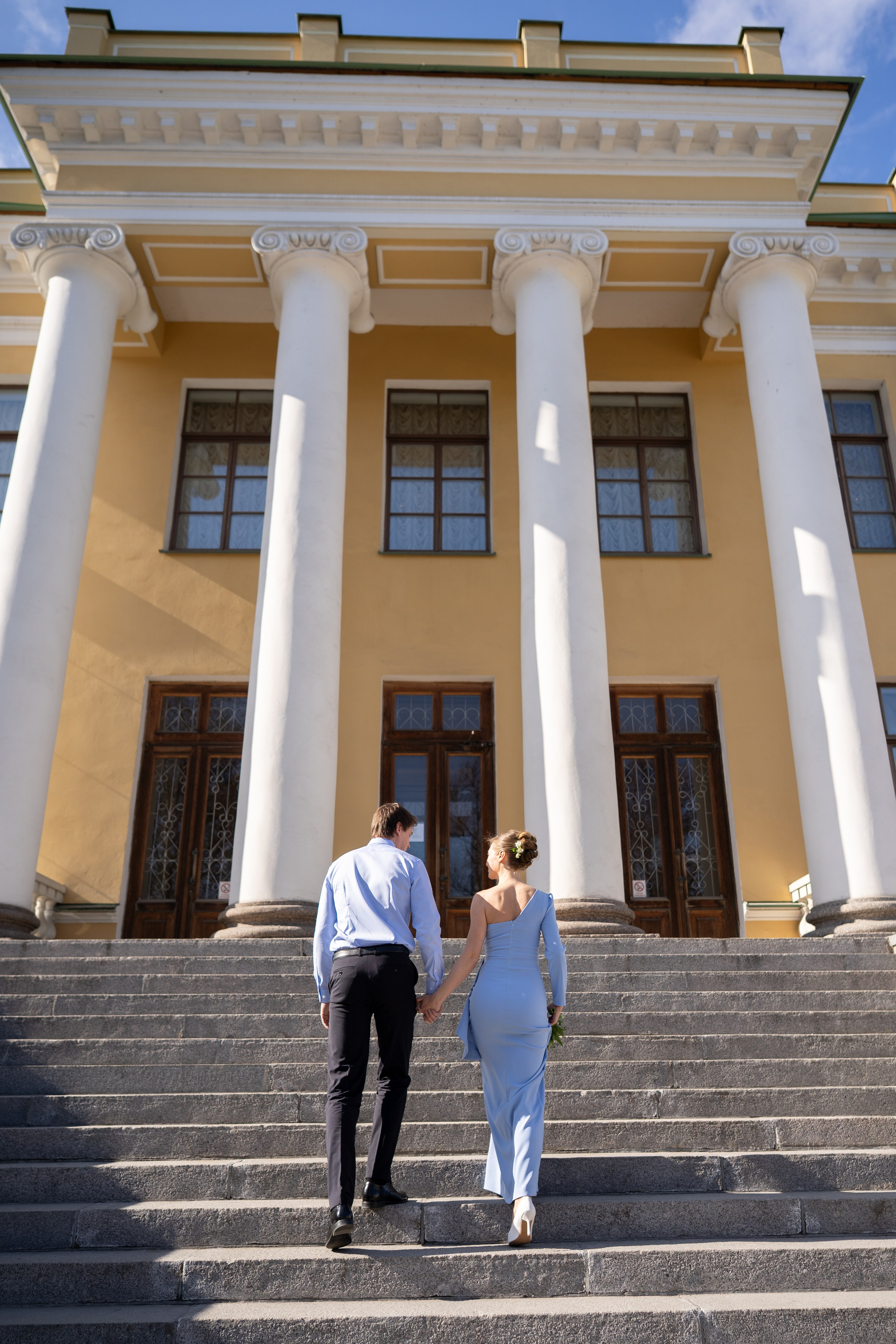 Свадебная фотосессия в ЗАГСе Кировского района. Жених и невеста поднимаются по лестнице на улице в двери загса