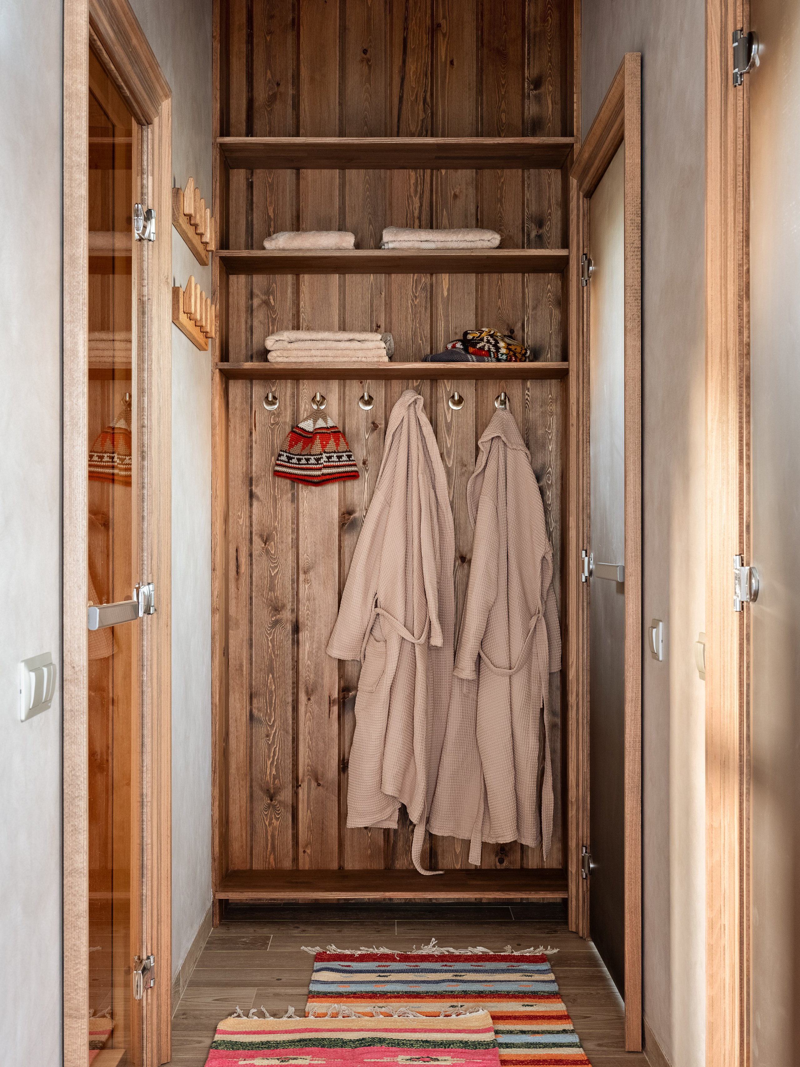 Функциональный гардеробный уголок с деревянными стенами, полками, халатами и вязанными шапками для сауны, оформленный дизайнером Наталией Шелепниковой, стилистом Софией Калбазовой и снятый фотографом Сергеем Денисенко в аутентичном стиле.