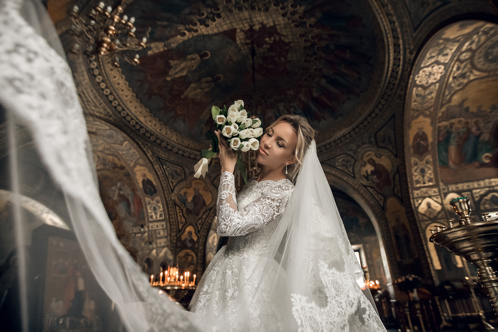портрет невесты в храме с букетом белых тюльпанов и разлетающейся фатой
