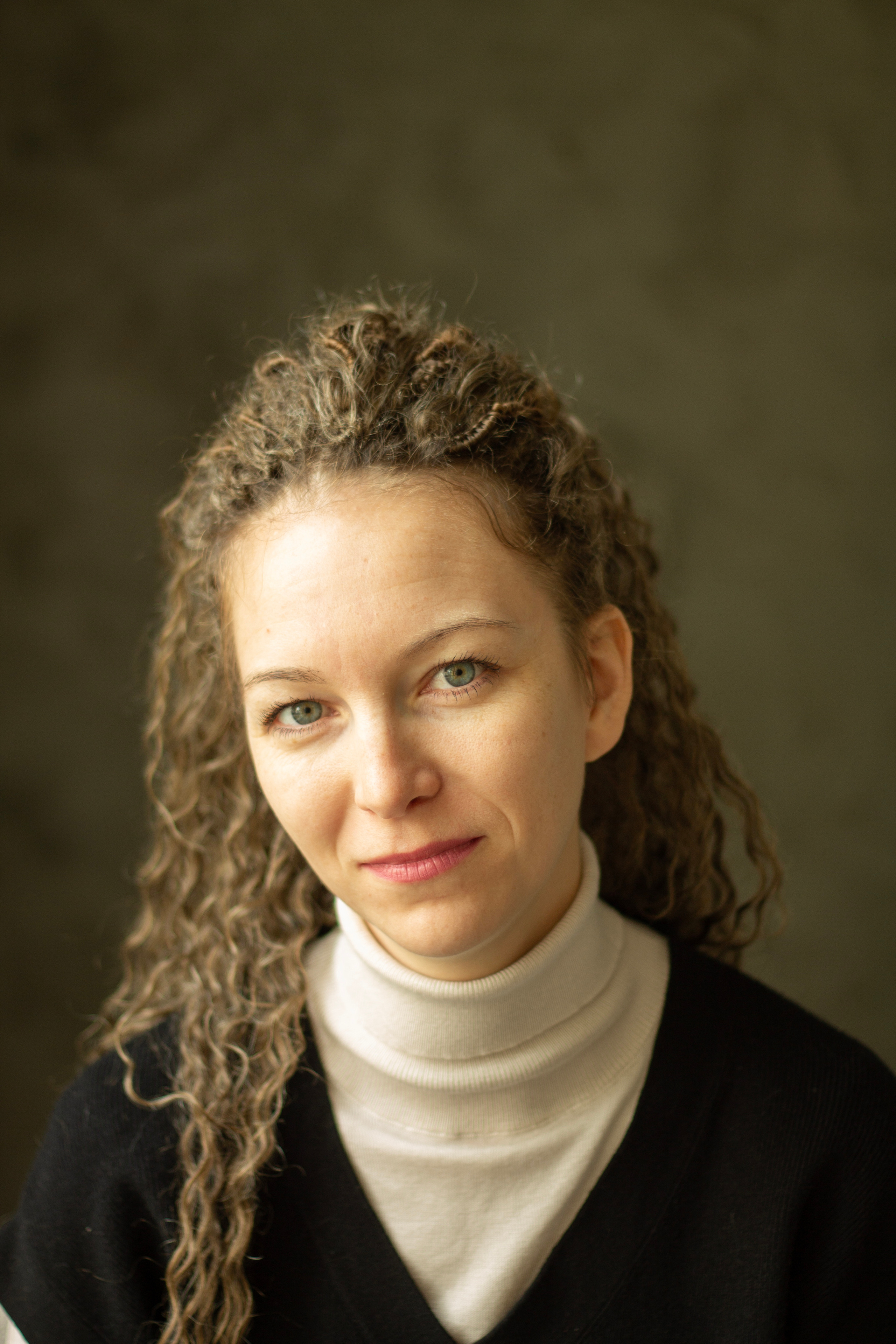 Портрет кудрявой девушки в белой водолазке и черном жилете