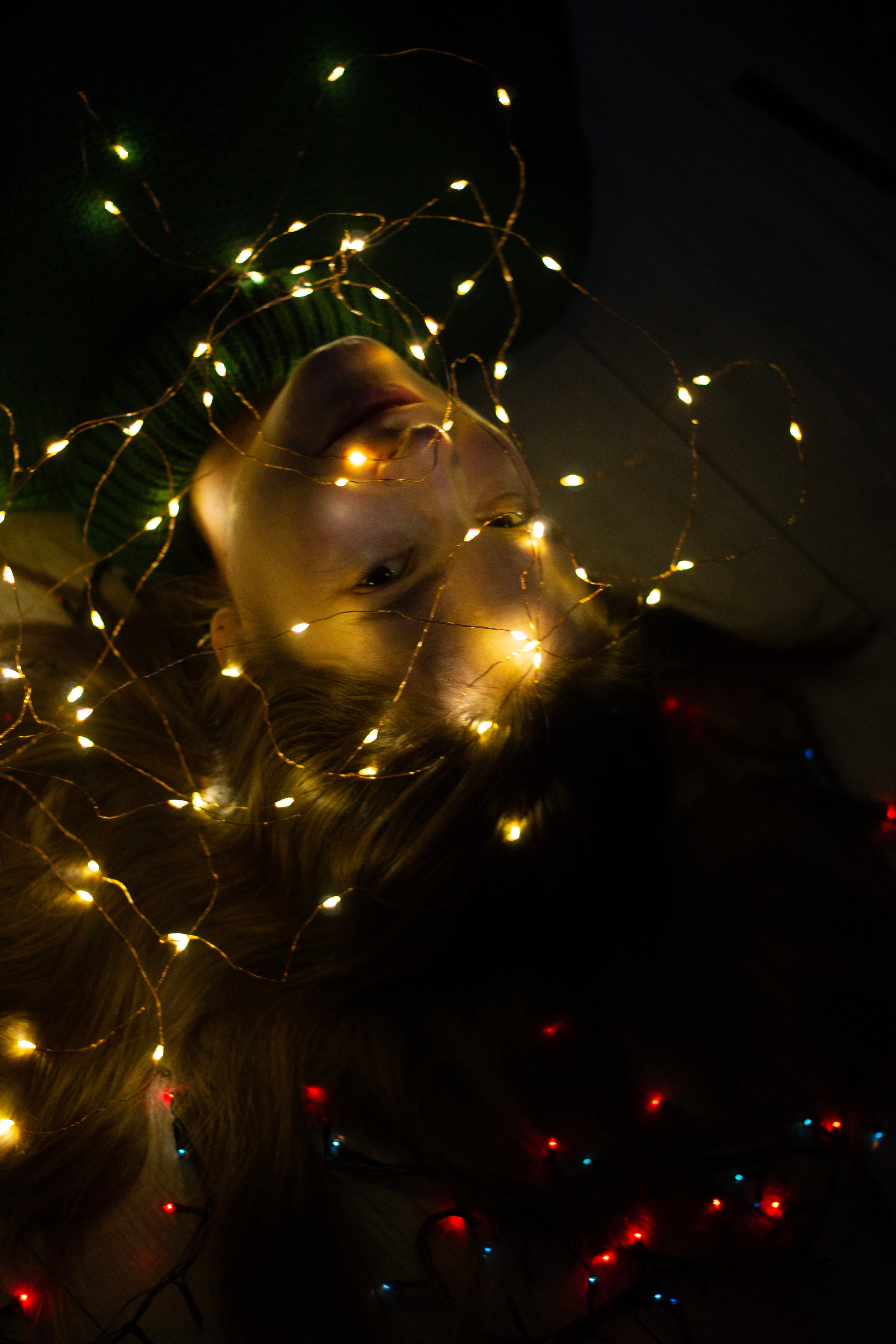 Девушка с распущенными волосами лежит на полу с новогодними фонариками