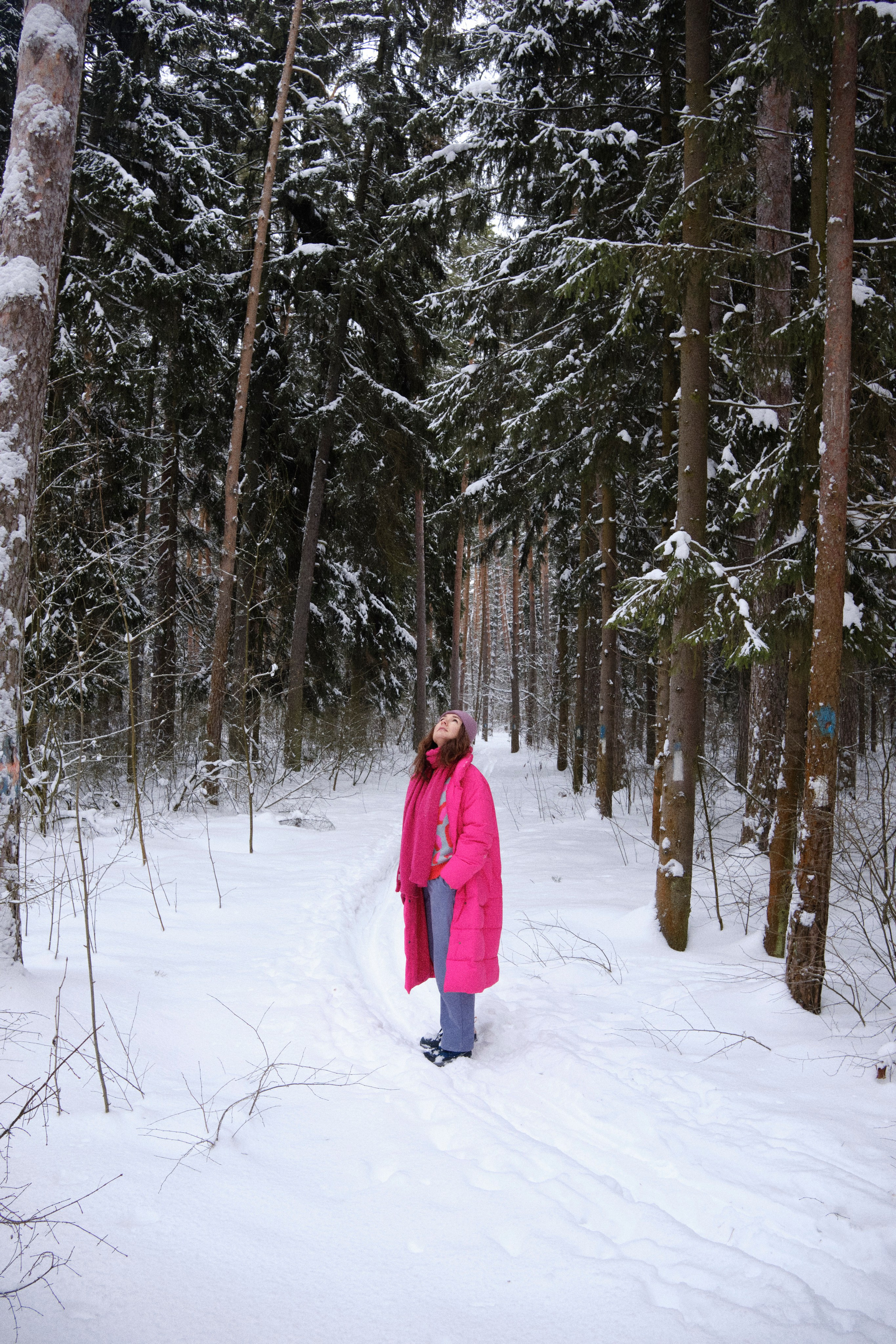 Женщина стоит в зимнем лесу в яркой одежде во весь рост