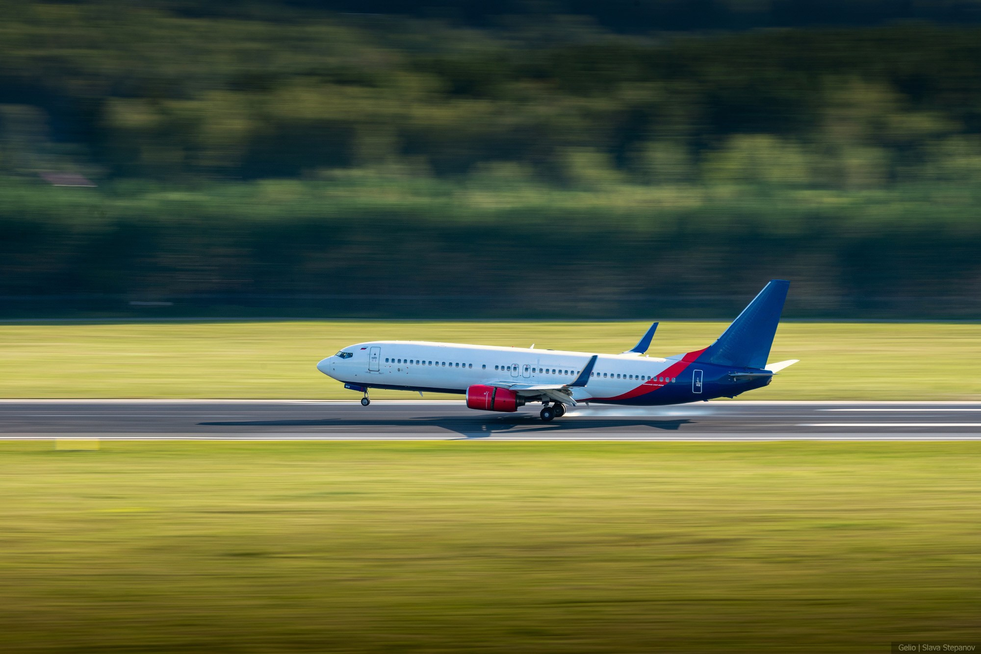Пассажирский самолет Boeing 737 на взлетно-посадочной полосе во время пробега. Съемка с эффектом проводки, размывающей задний план с зелеными деревьями. Снимок Gelio.