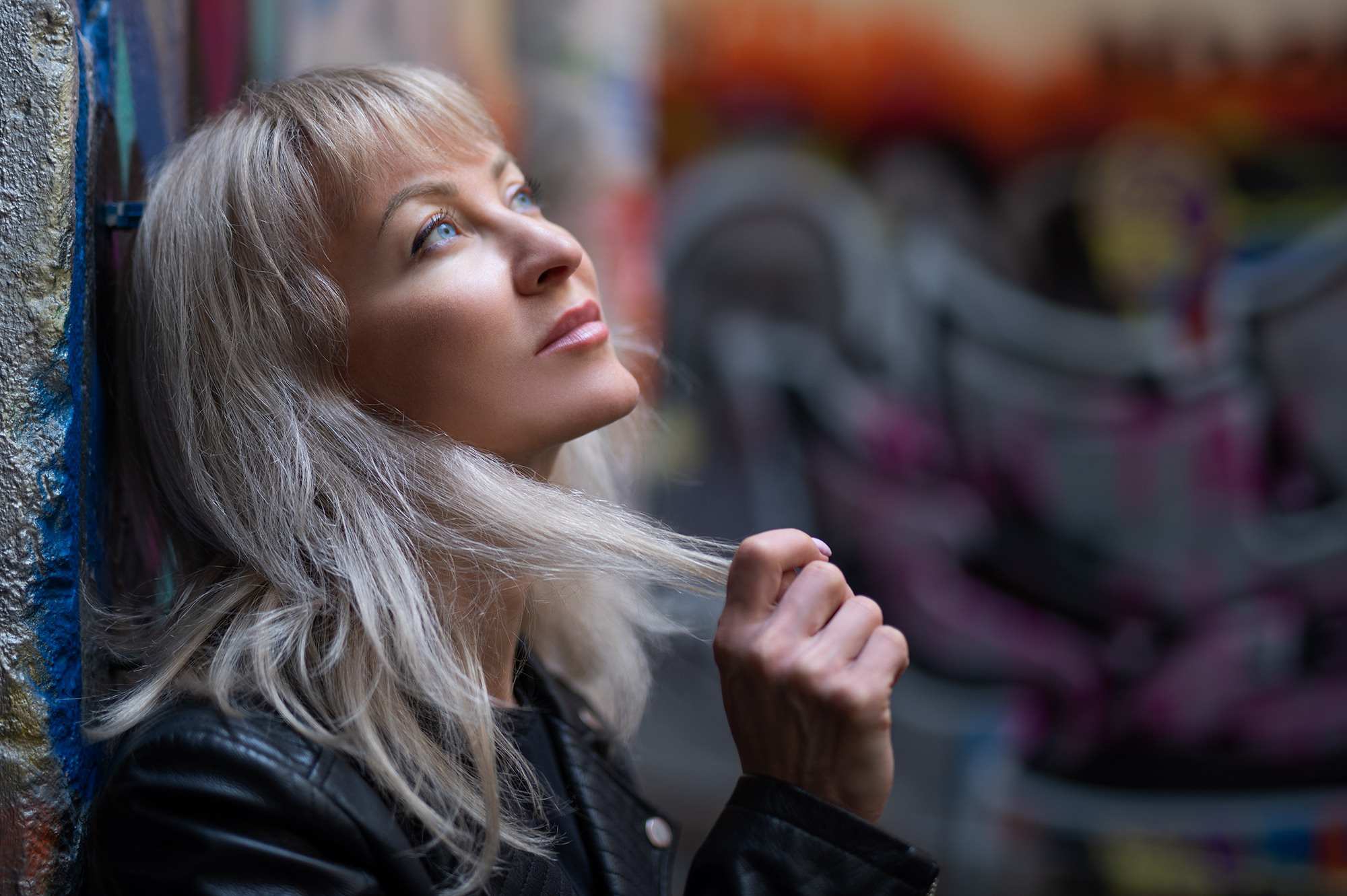 Блондинка с голубыми глазами в черной косухе на фоне граффити