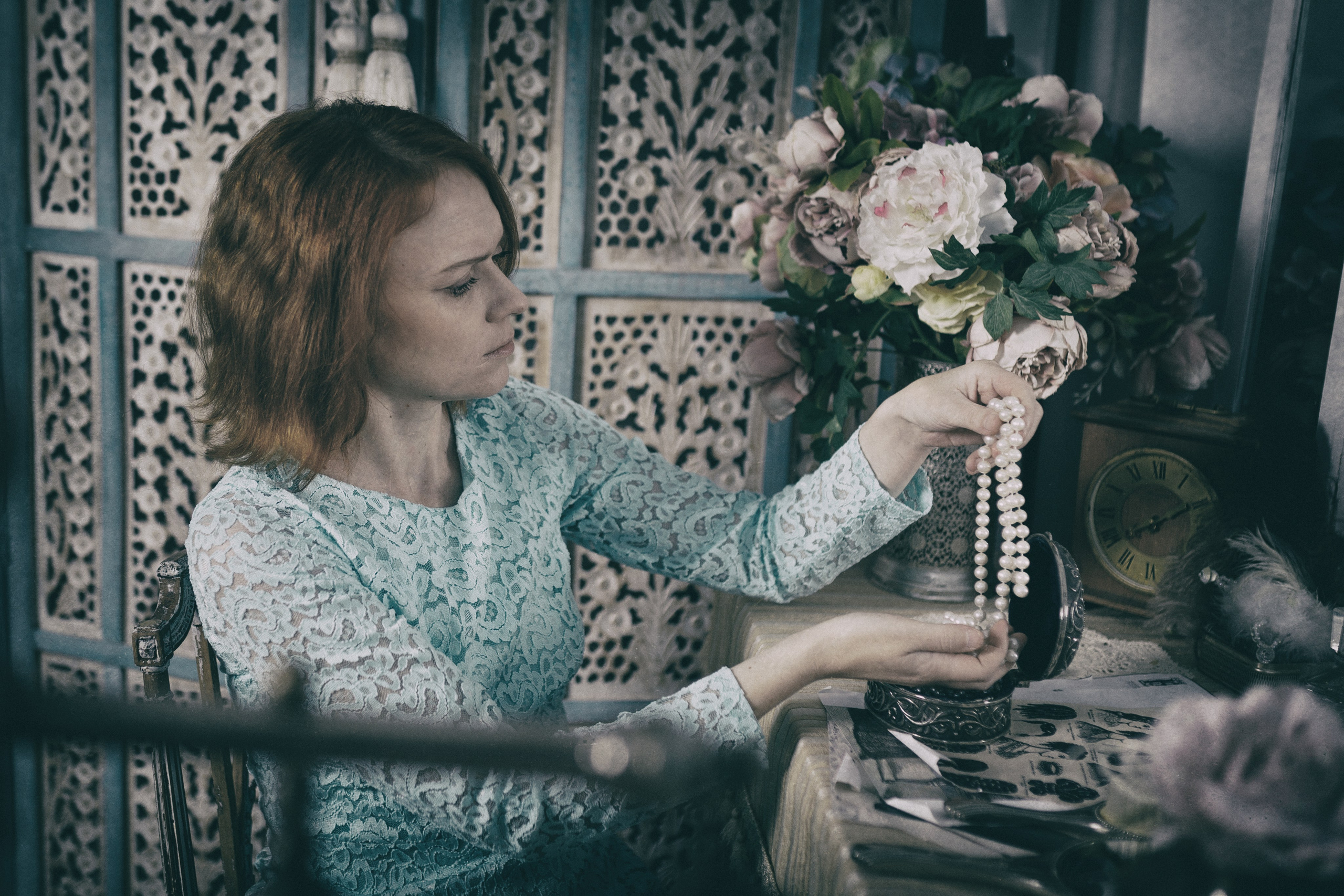 Рыжая девушка перебирает украшения на фоне ширмы