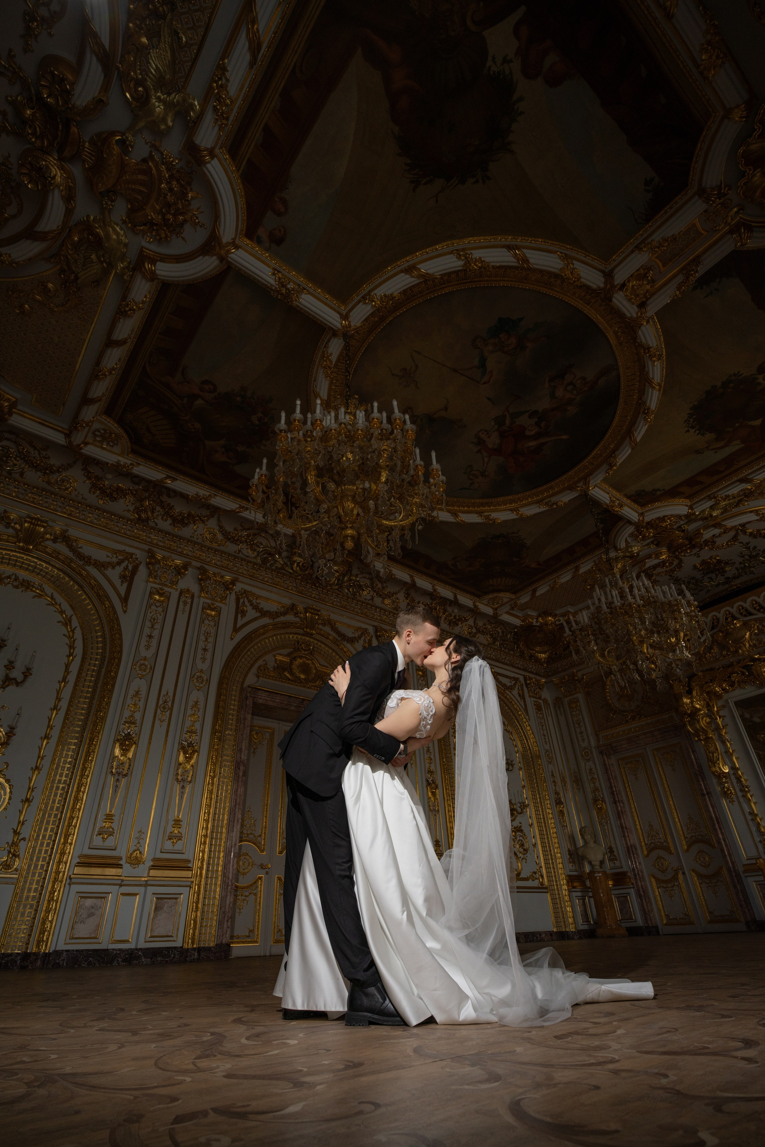 Свадебная фотосессия в Санкт-Петербурге в Особняке Половцева или Дом Архитектора. Жених красиво целует невесту с прогибом и фата летит в золотом зале с красивыми люстрами