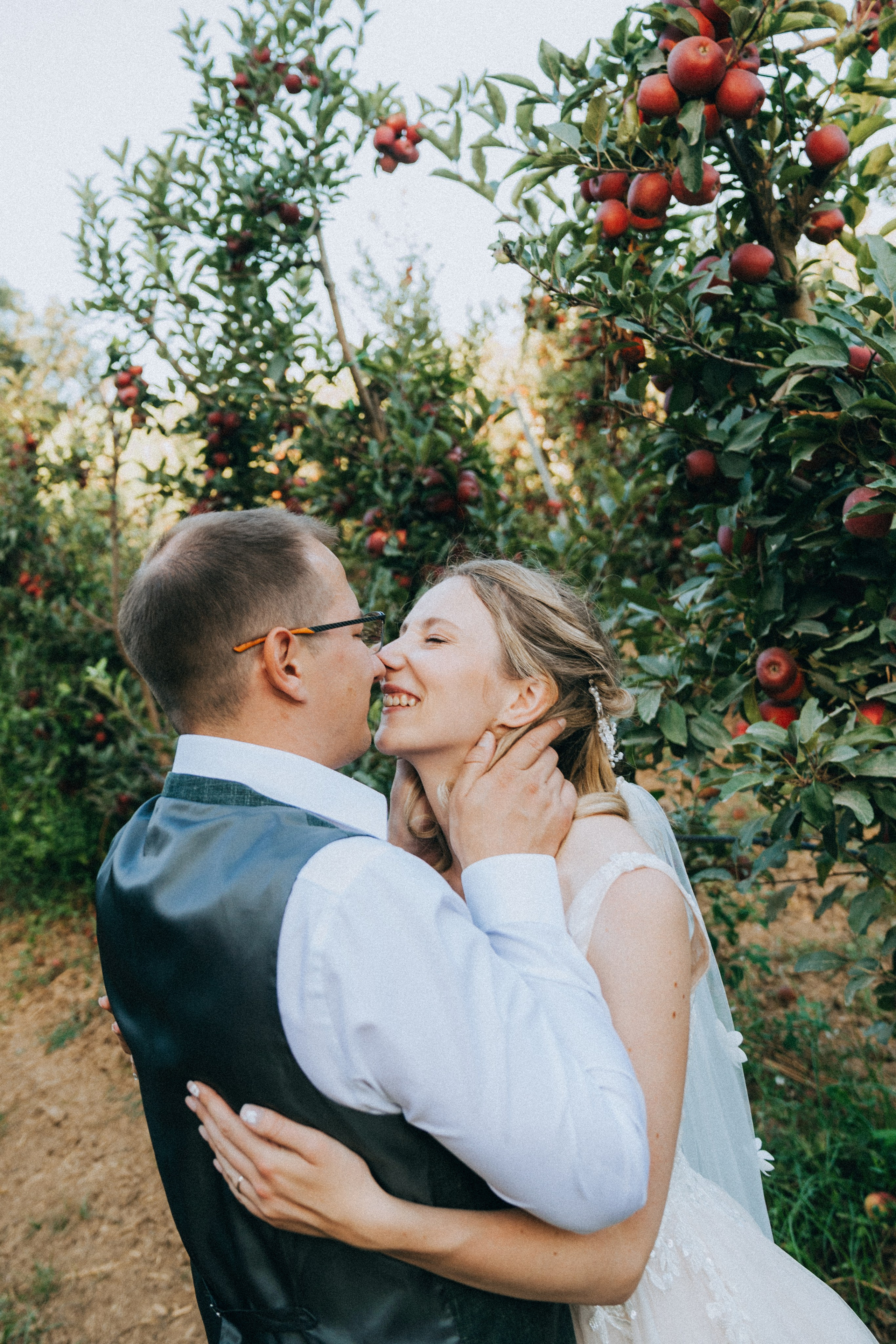 Жених и невеста обнимаются среди яблоневого сада, вокруг созревшие яблоки.