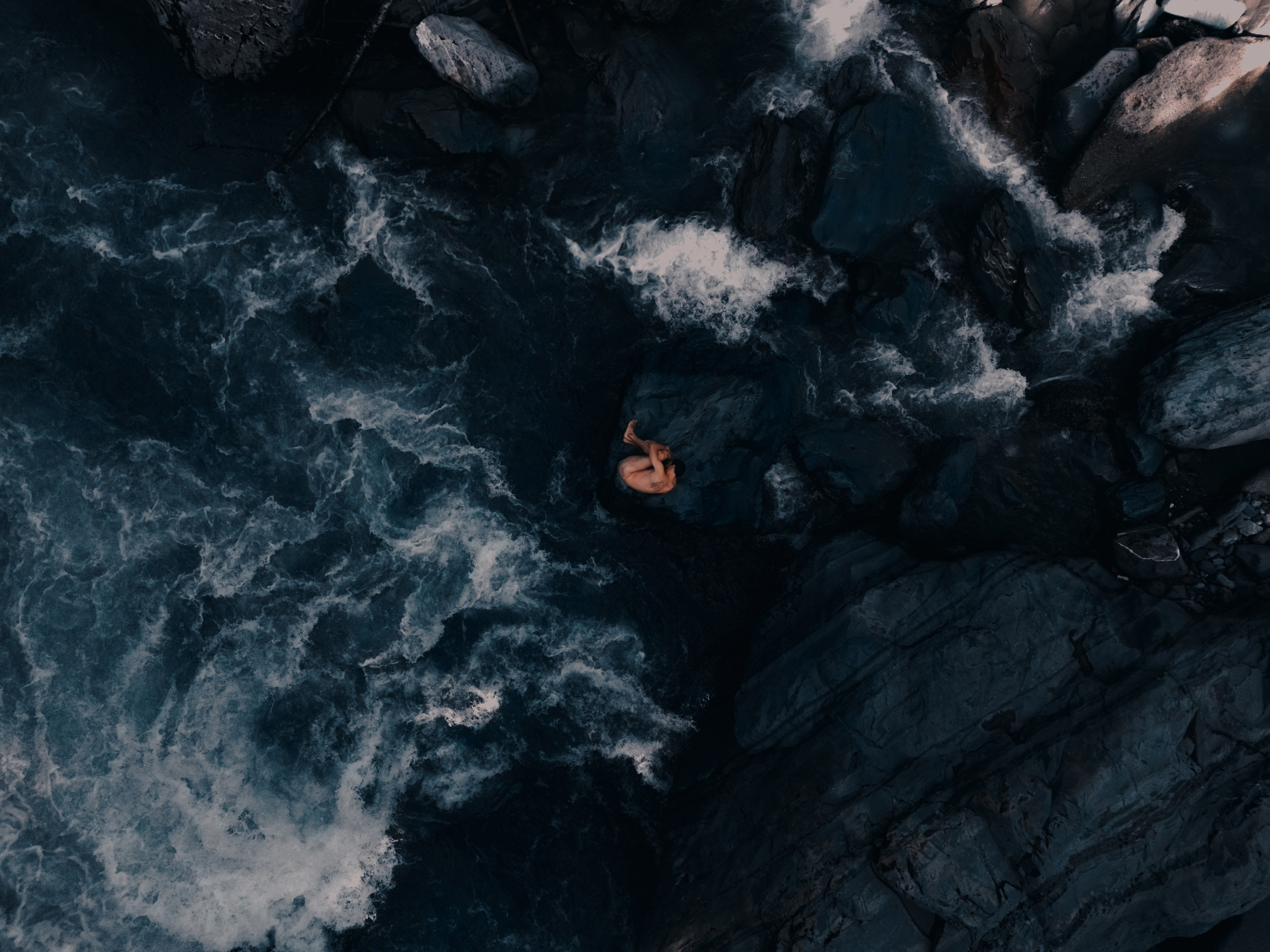 Съемка парня сверху с коптера на фоне реки и камней