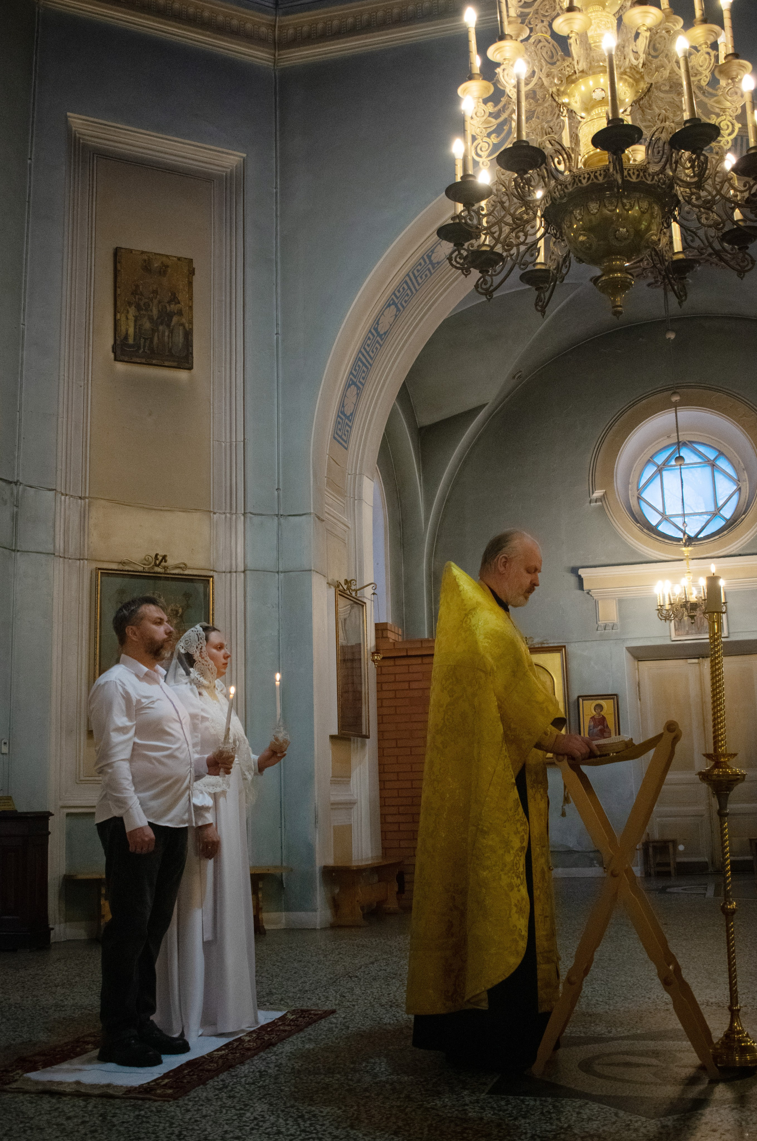 Венчание в Сортавала, Карелия. Фотосъемка в никольском храме, молодожены держат свечи, священник читает молитву.