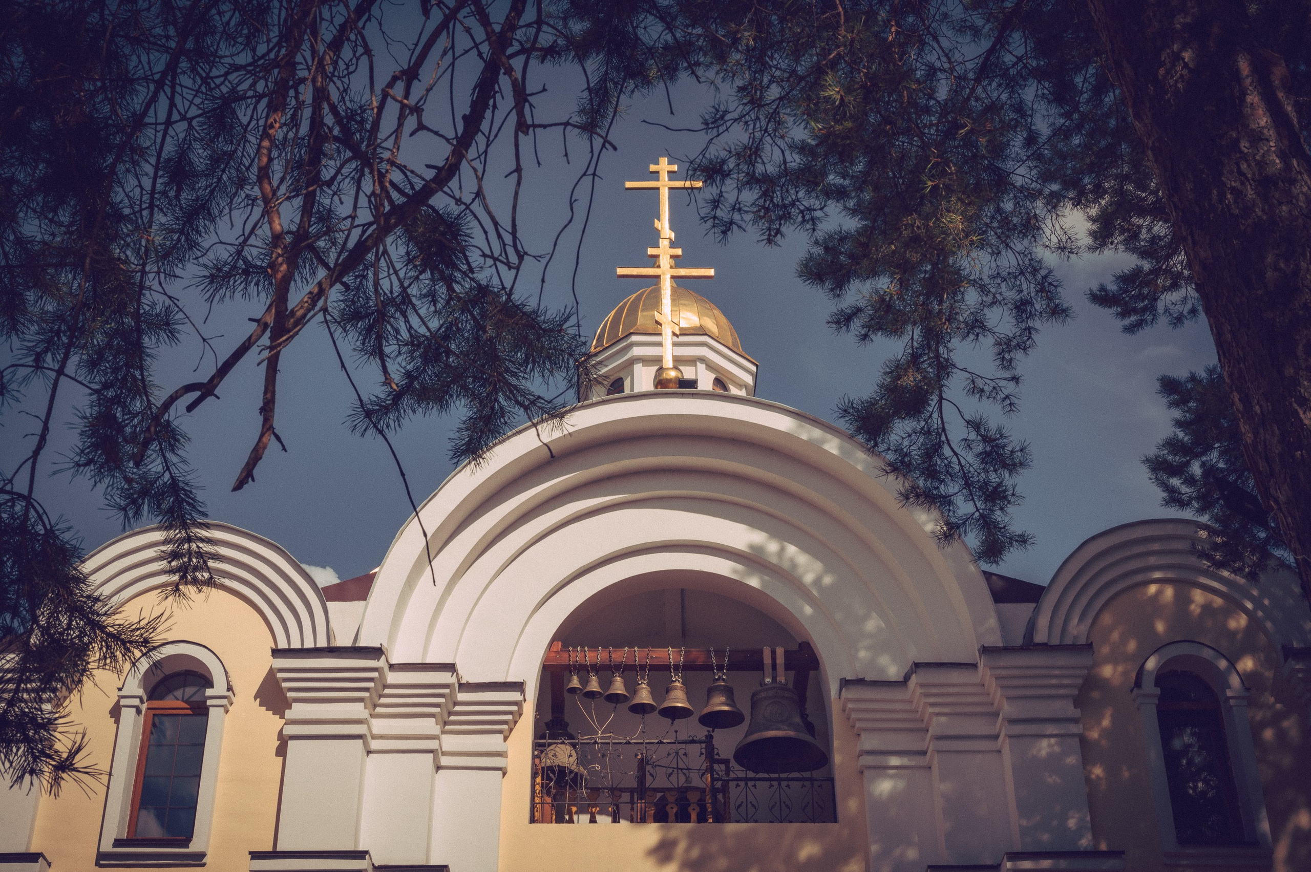 церковь крест купол на фоне неба через листву колокола