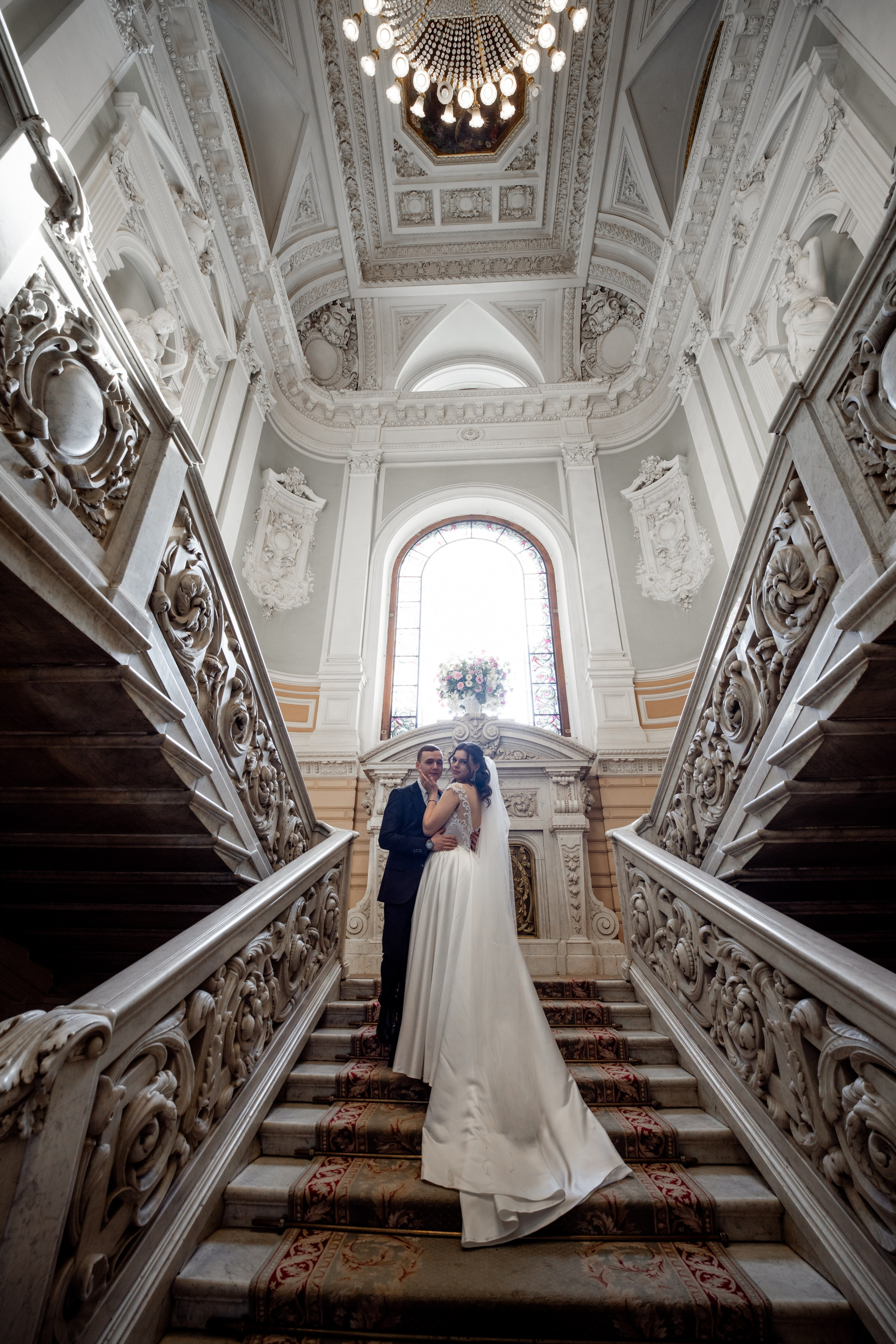 Свадебная фотосессия в Санкт-Петербурге во дворце  бракосочетания №1 на Английской набережной. Невеста и жених стоят на  лестнице. Видна вся лестница и люстра.