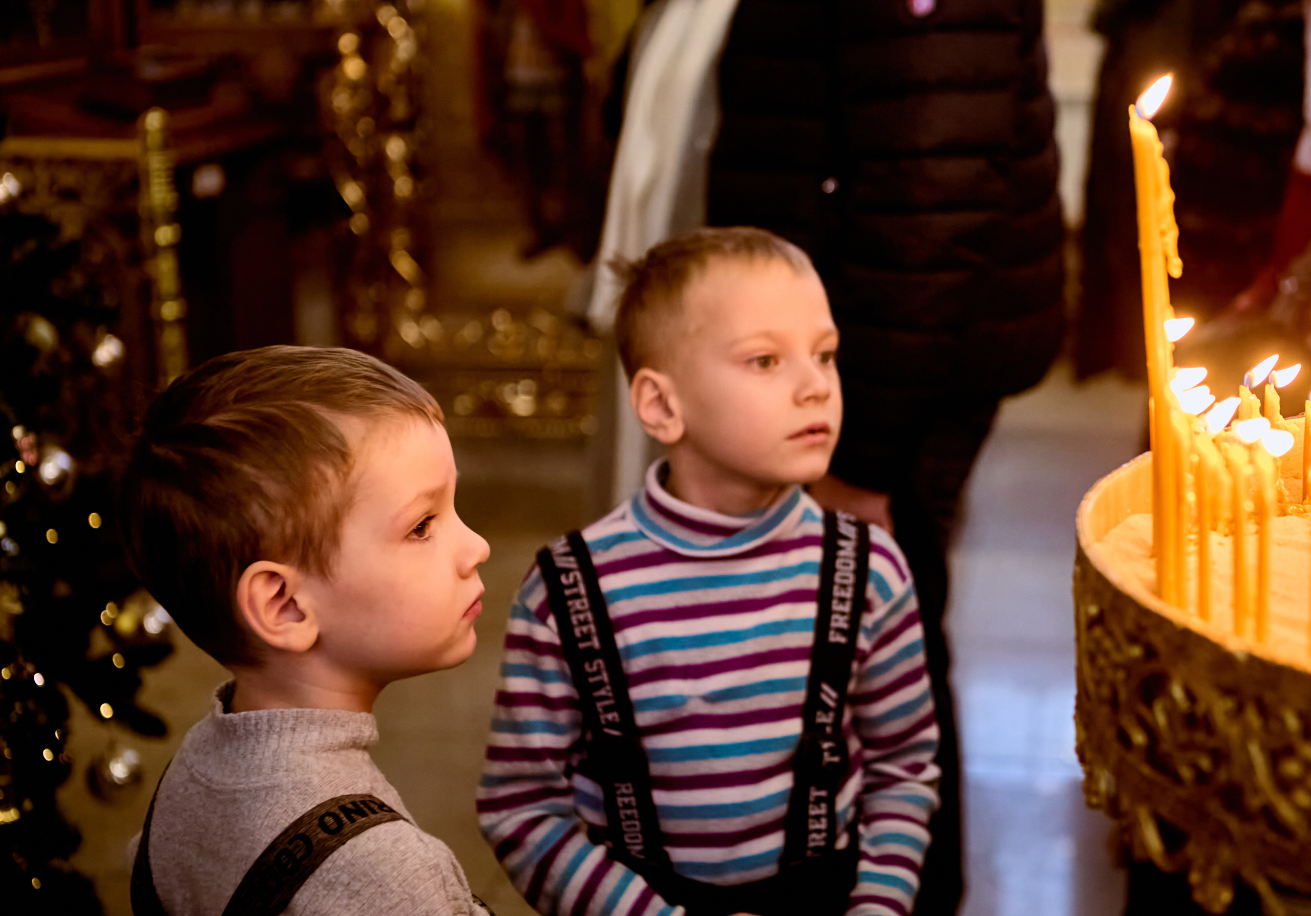 Два маленький братика стоят у подсвечника помогают.