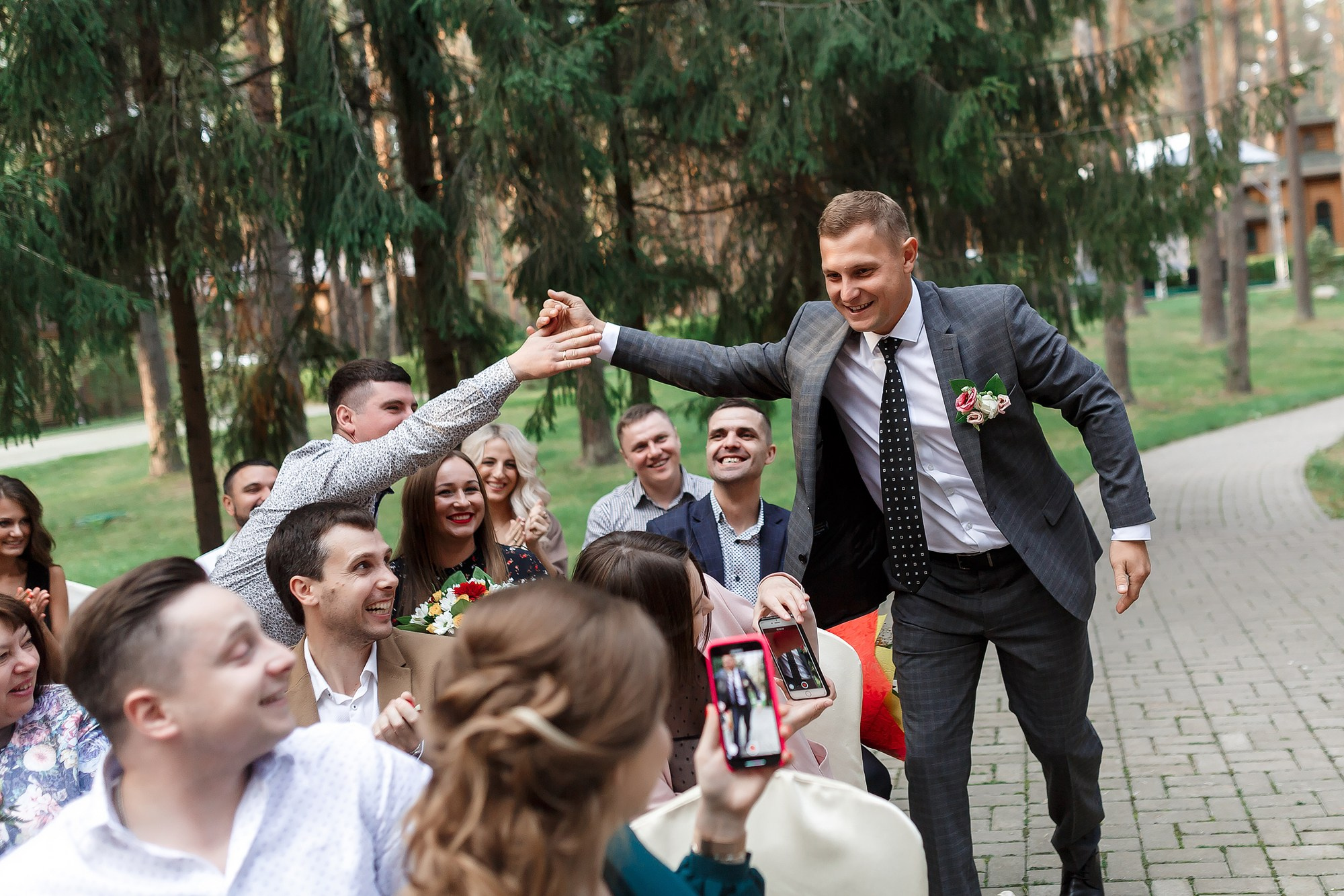 Счастливый улыбающийся жених приветствует гостей на выездной церемонии бракосочетания в загородном парк-отеле