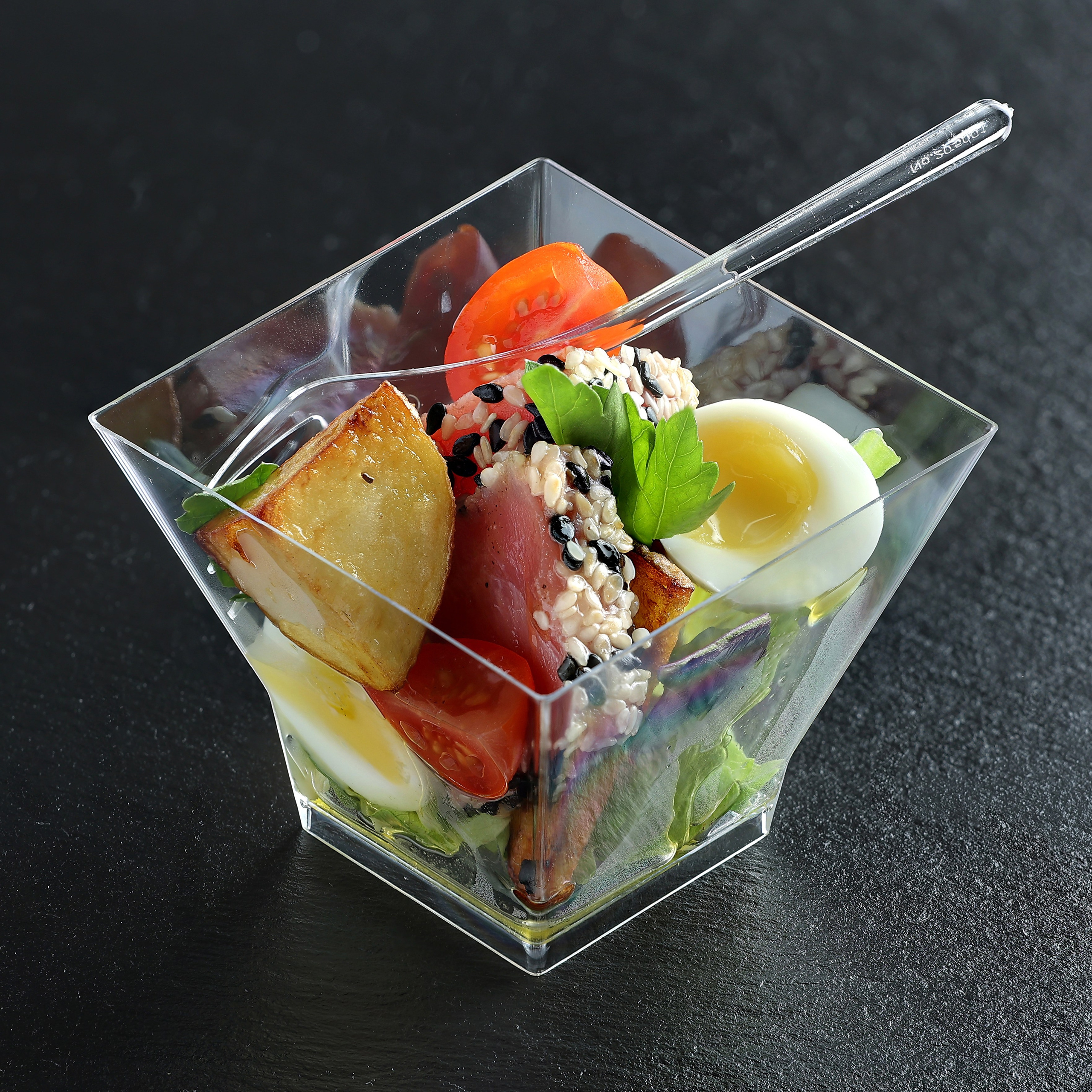 Салат с запечённым тунцом, перепелиным яйцом, картофелем по-деревенски и черри в прозрачной пиалке с вилочкой.