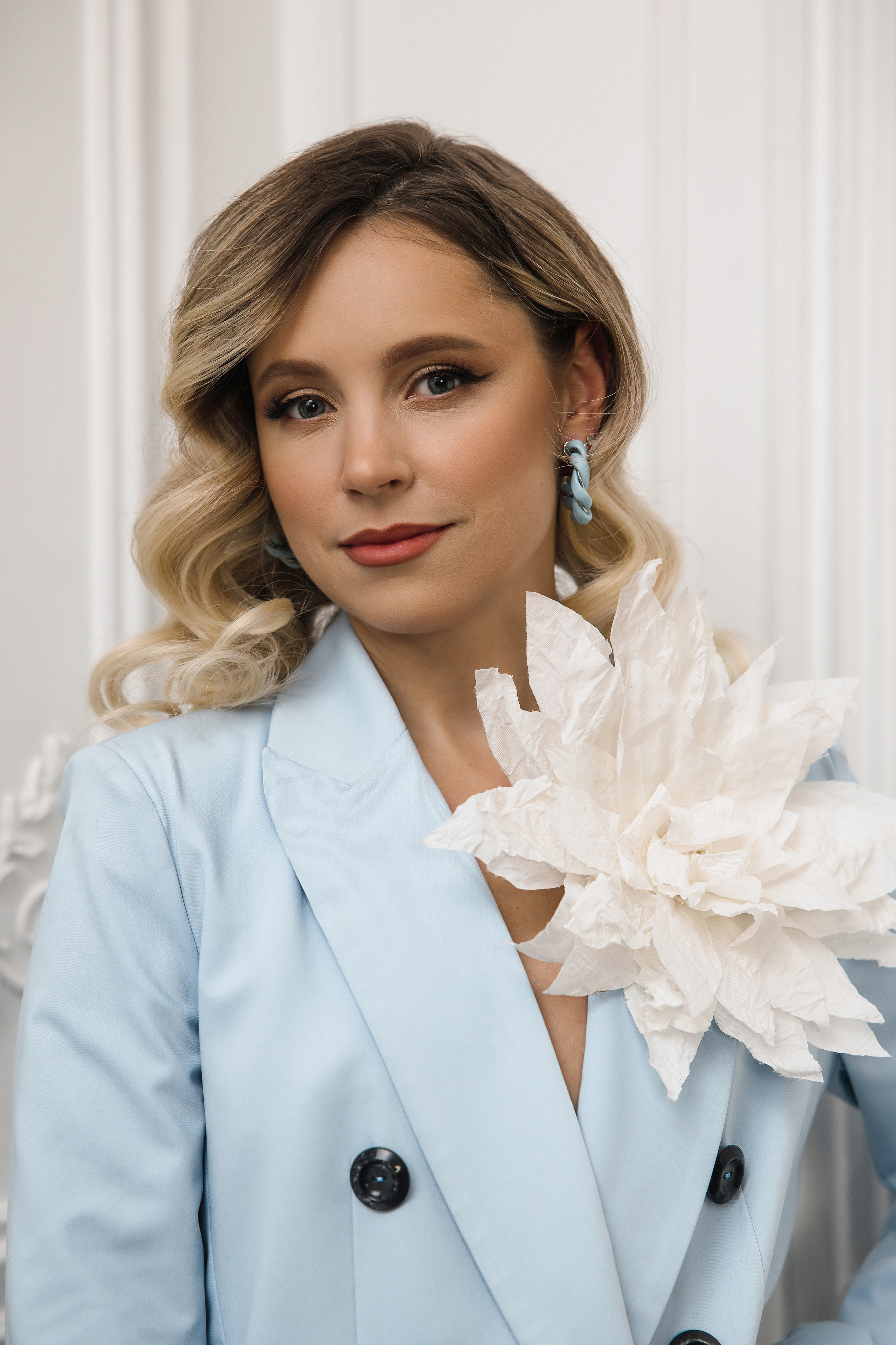 Портрет девушки блондинки с кудрямит и большим белым цветком на шее.