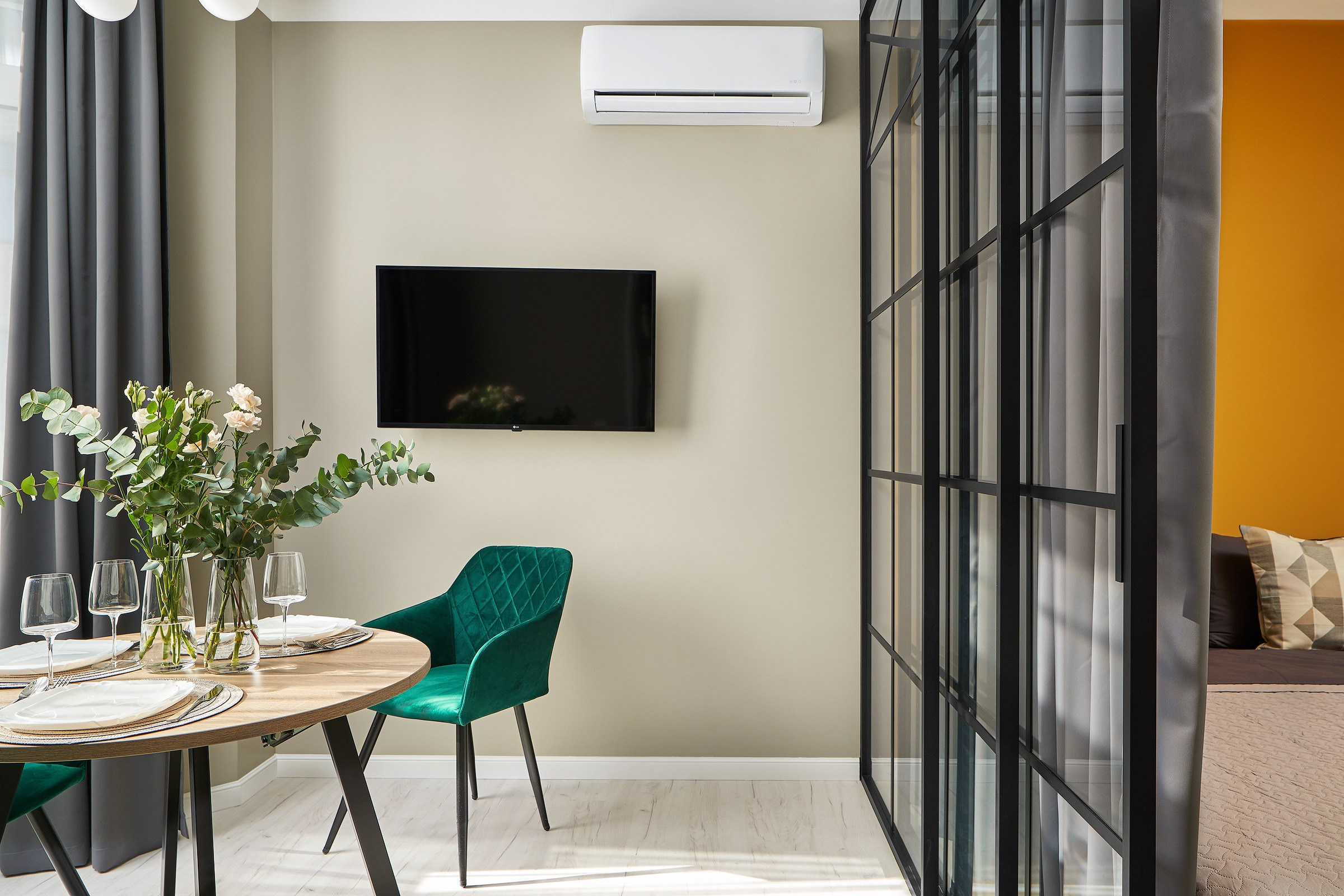 Гостиная совмещенная с спальней, стеклянная железная перегородка, стол с цветами и зеленый стул 