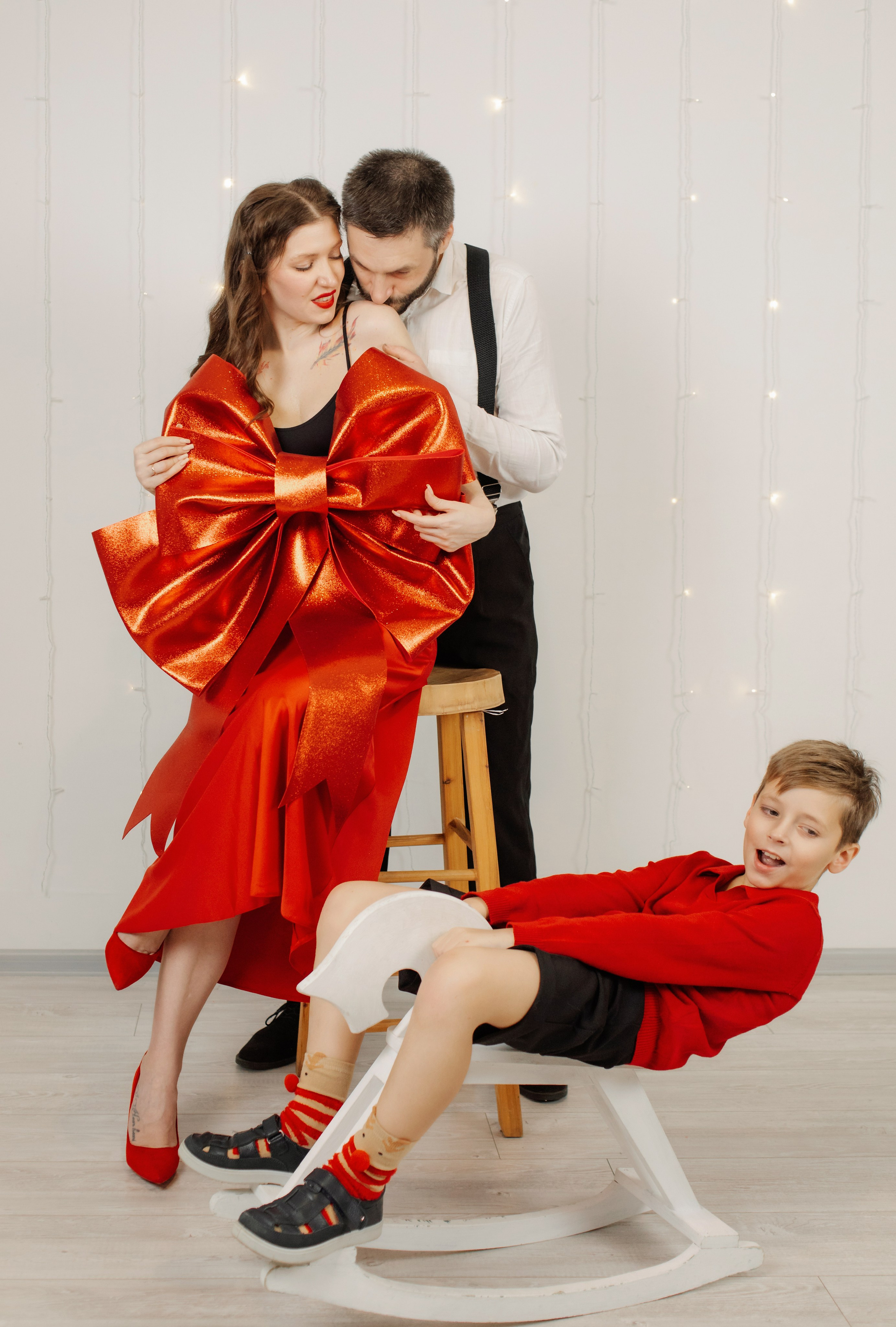 семейная новогодняя минималистичная фотосессия в студии в черно бело красной гамме, мальчик на лошадке