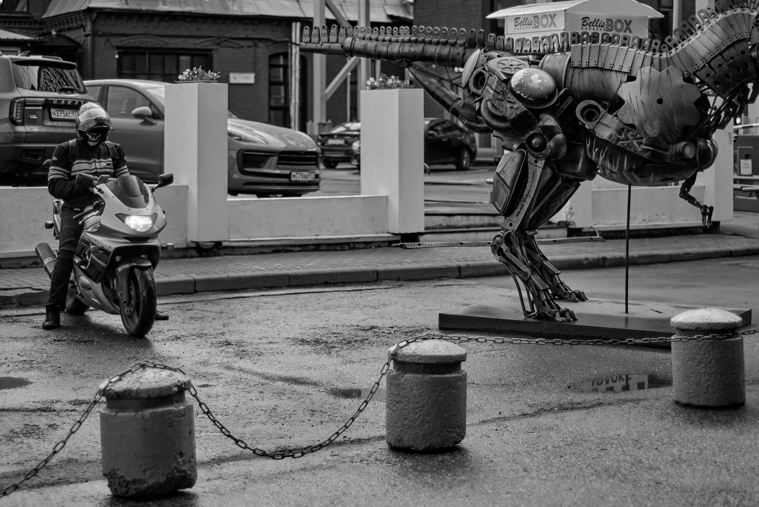 Мотоциклист в шлеме стоит рядом с тираннозавром. 