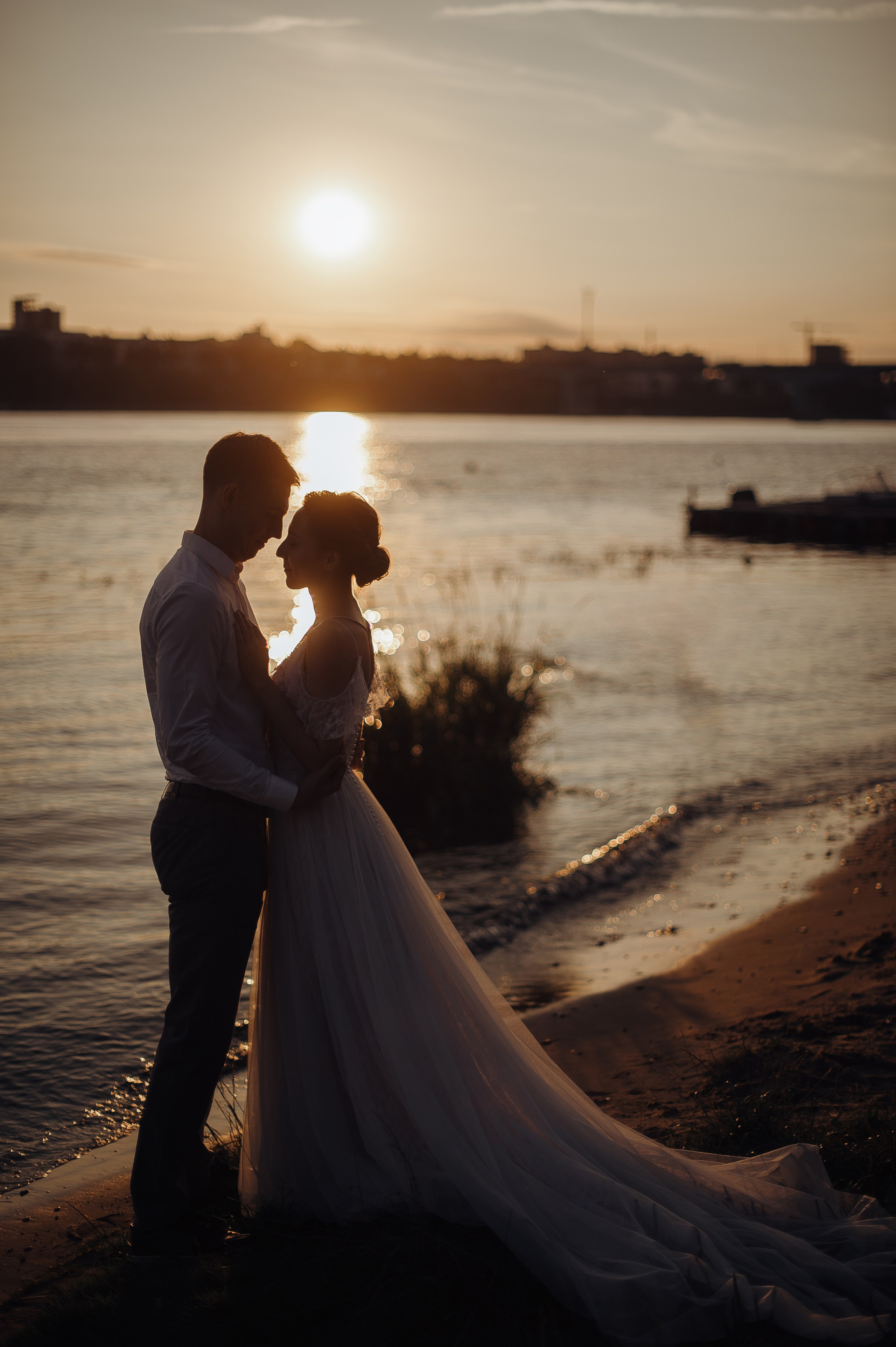 Влюбленные молодожены целуются на фоне закатного неба