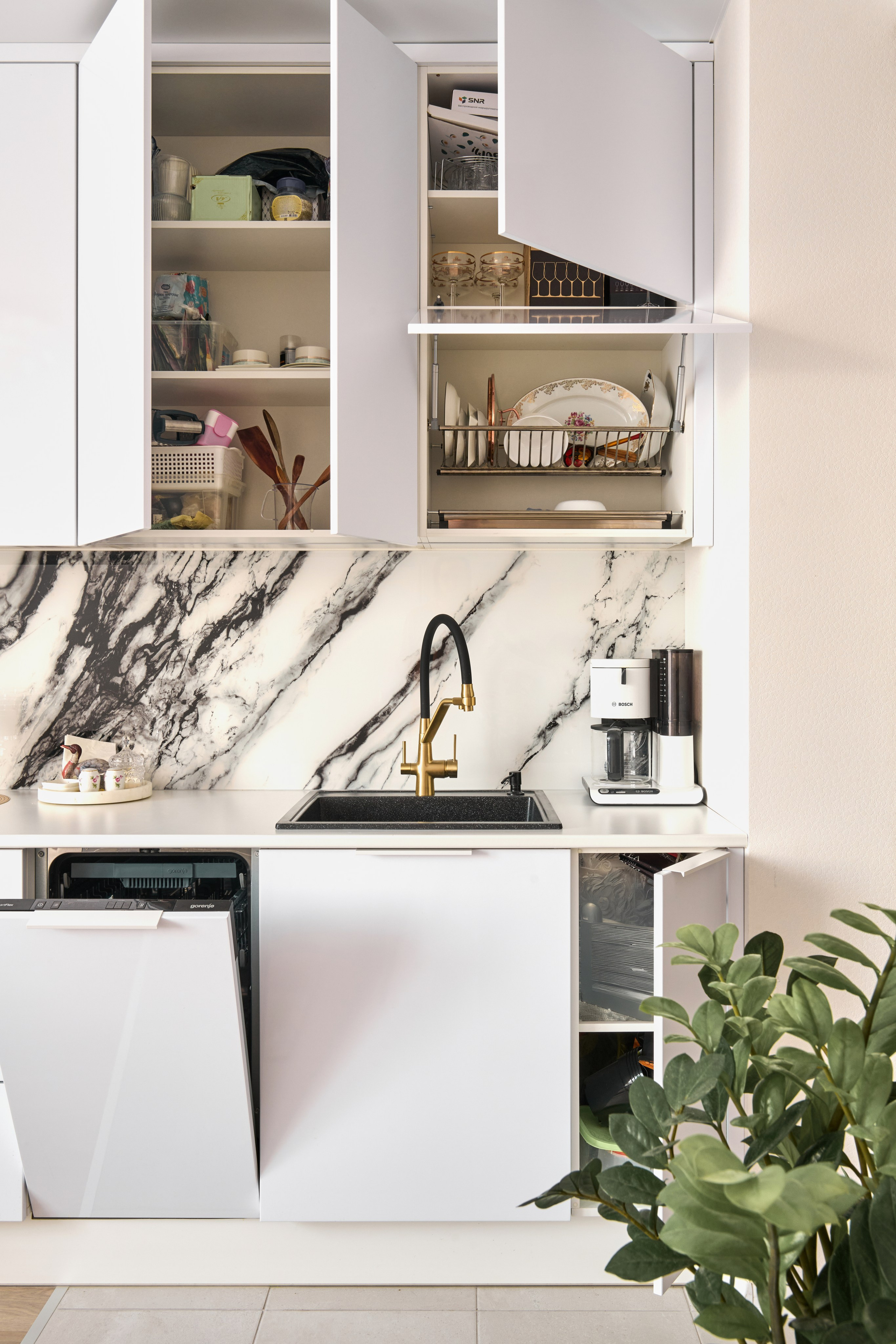 Белая кухня с мраморным фартуком, верхние шкафы, растение