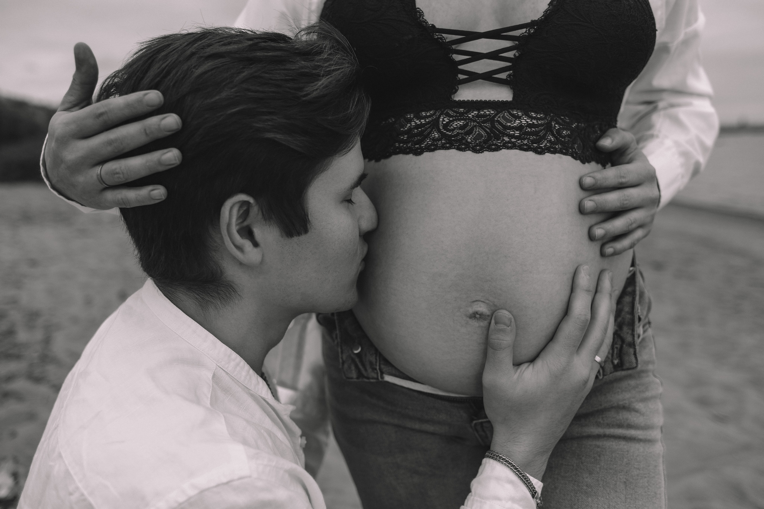 Пара у воды, девушка стоит, мужчина сидит на песке