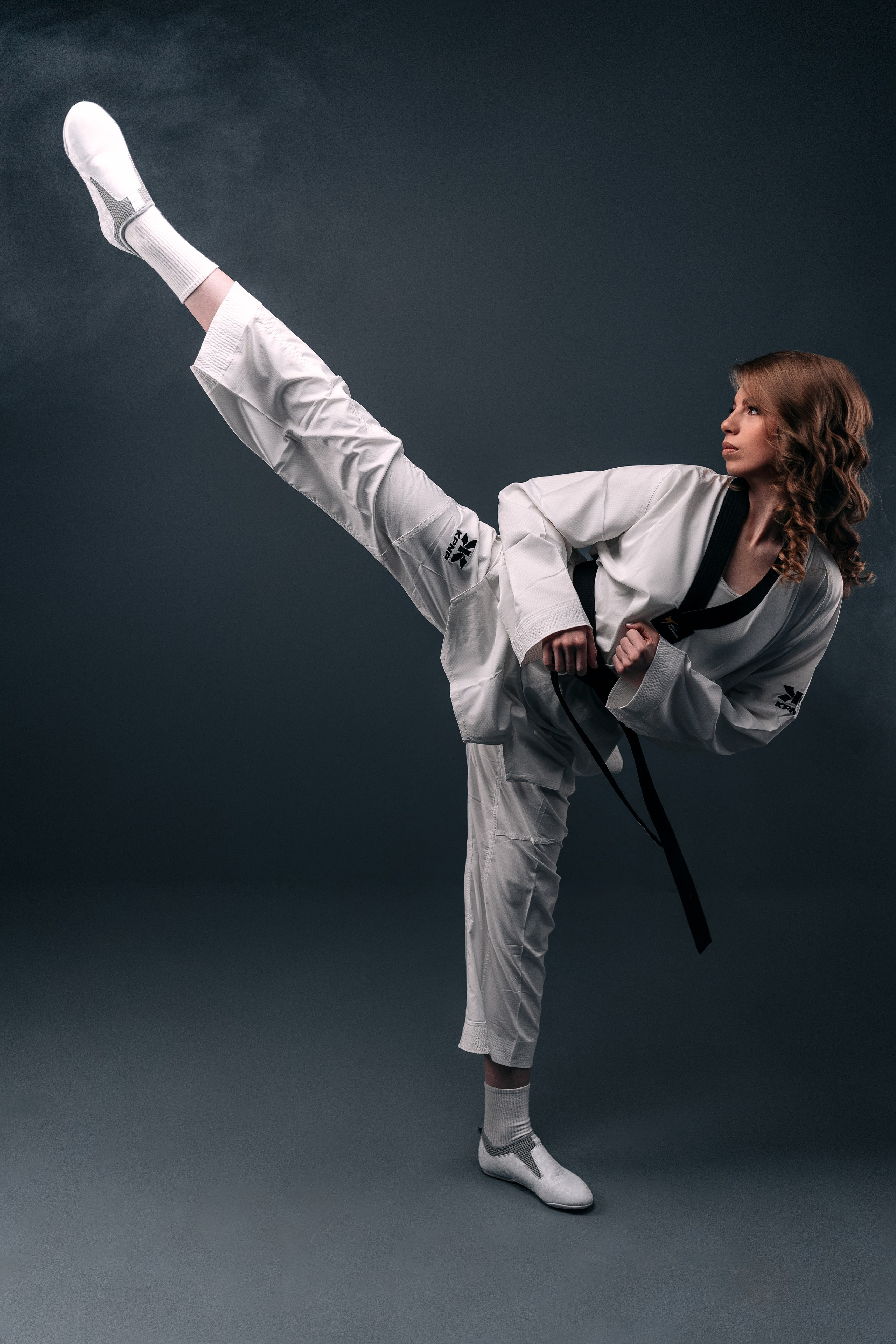 Девушка тхэквондистка, одетая в белое кимоно показывает верхний удар.