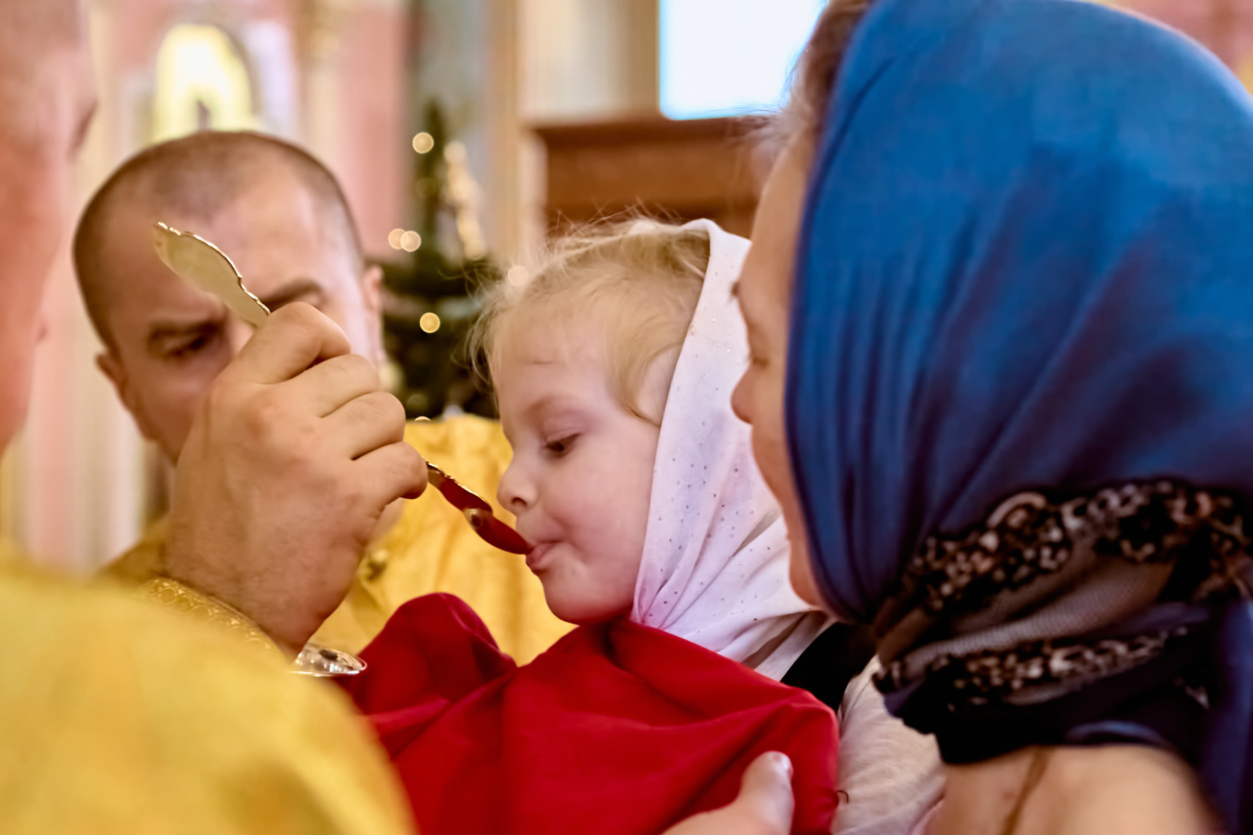 Маленькая девочка у мамы на руках причащается Святых Христовых таинств