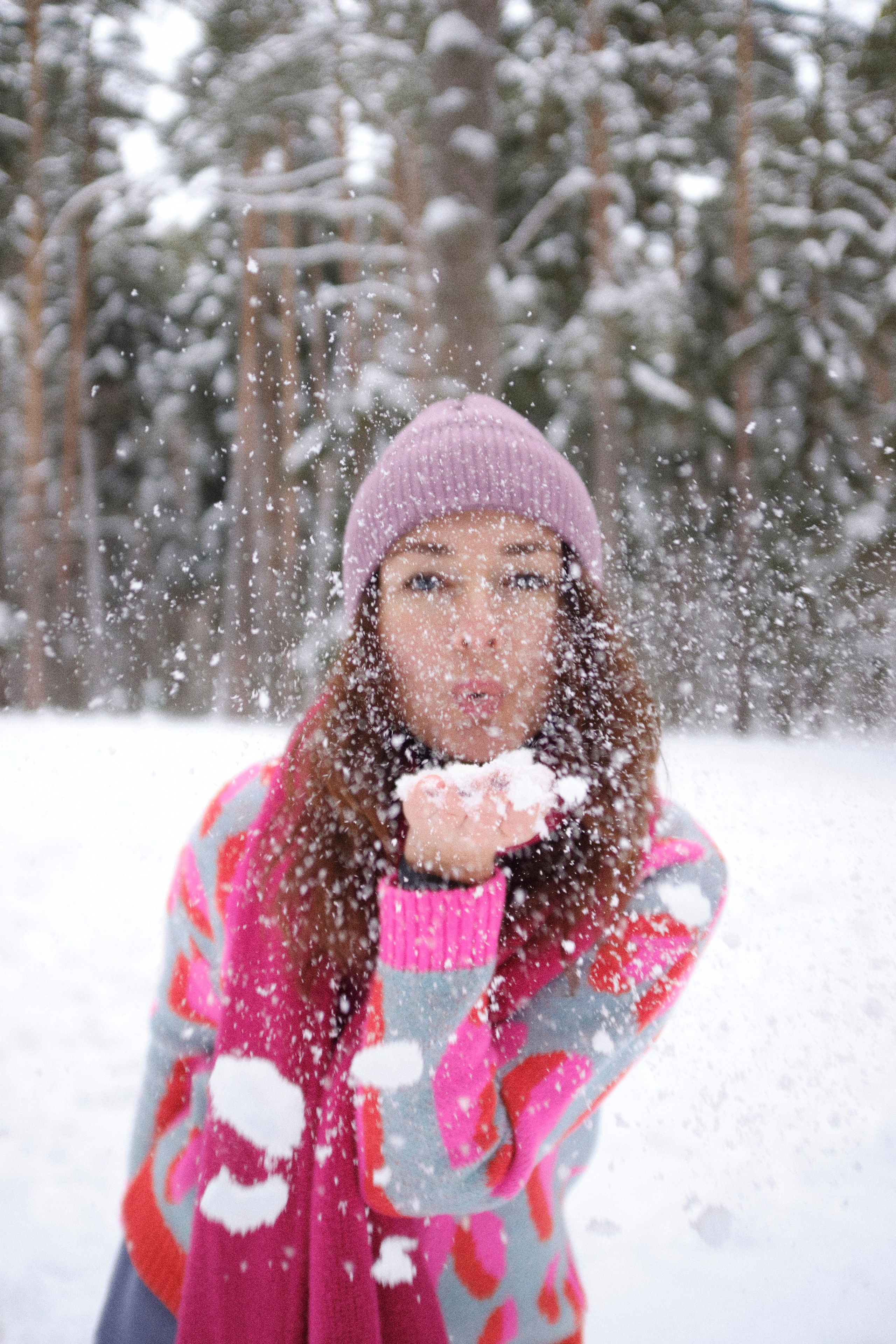 Женщина в яркой одежде в зимнем лесу сдувает снежинки с ладони