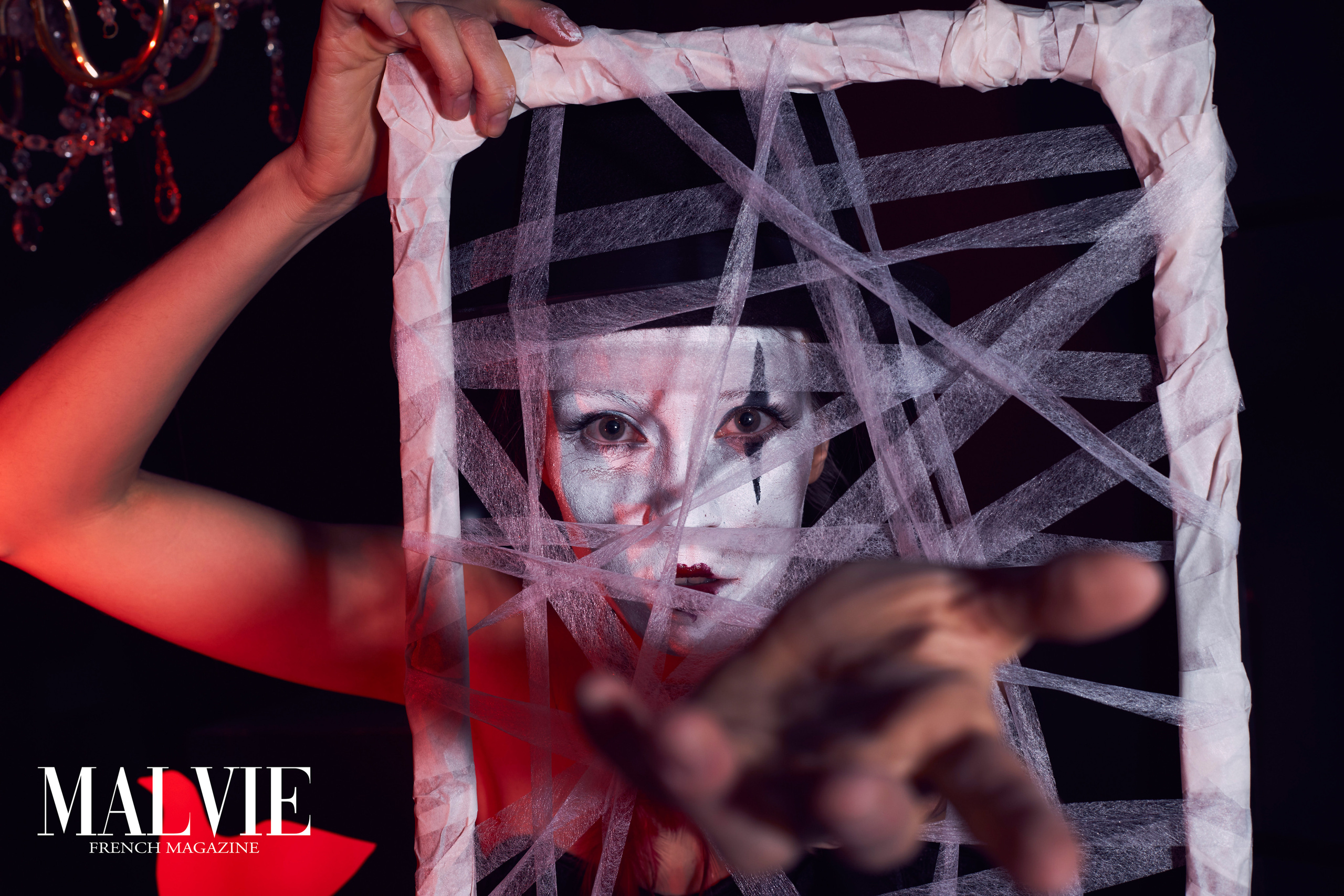 Художественный портрет девушки-клоуна, протягивающей руку сквозь картину с паутинками