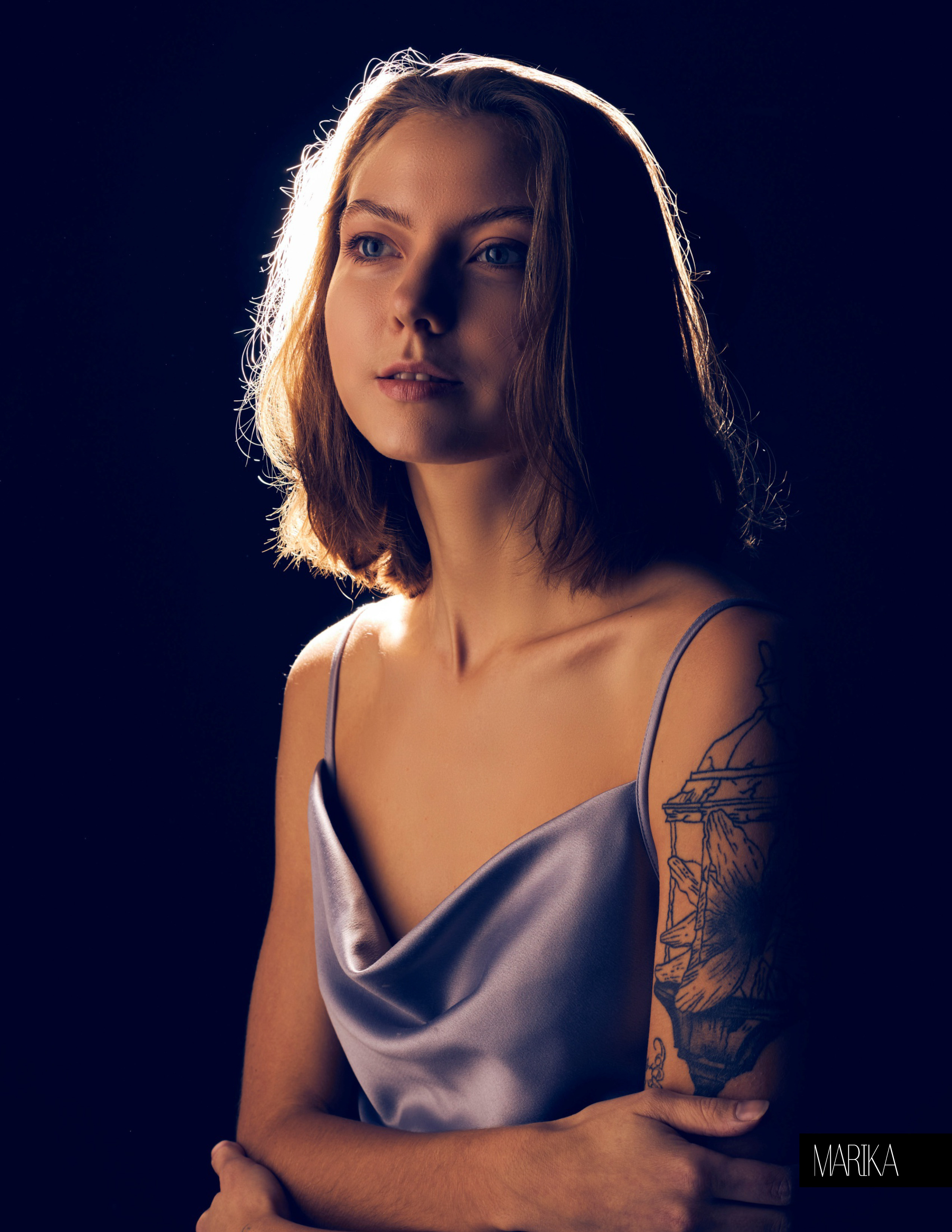 Портрет девушки с татуировкой на плече на тёмном фоне с контровым светом