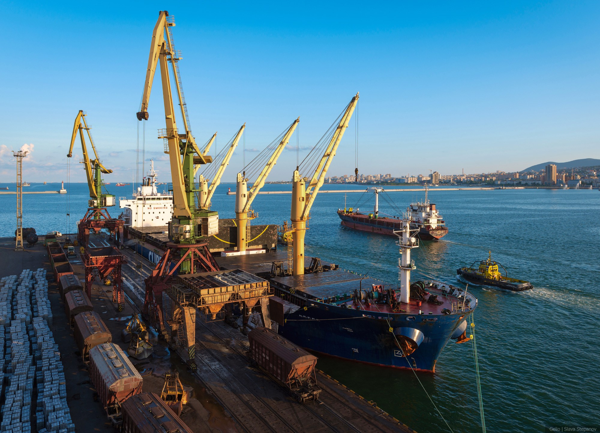 Высокие портальные краны обслуживают крупное грузовое судно у причала морского порта, индустриальный пейзаж с терминалом на фоне вечернего неба, Gelio