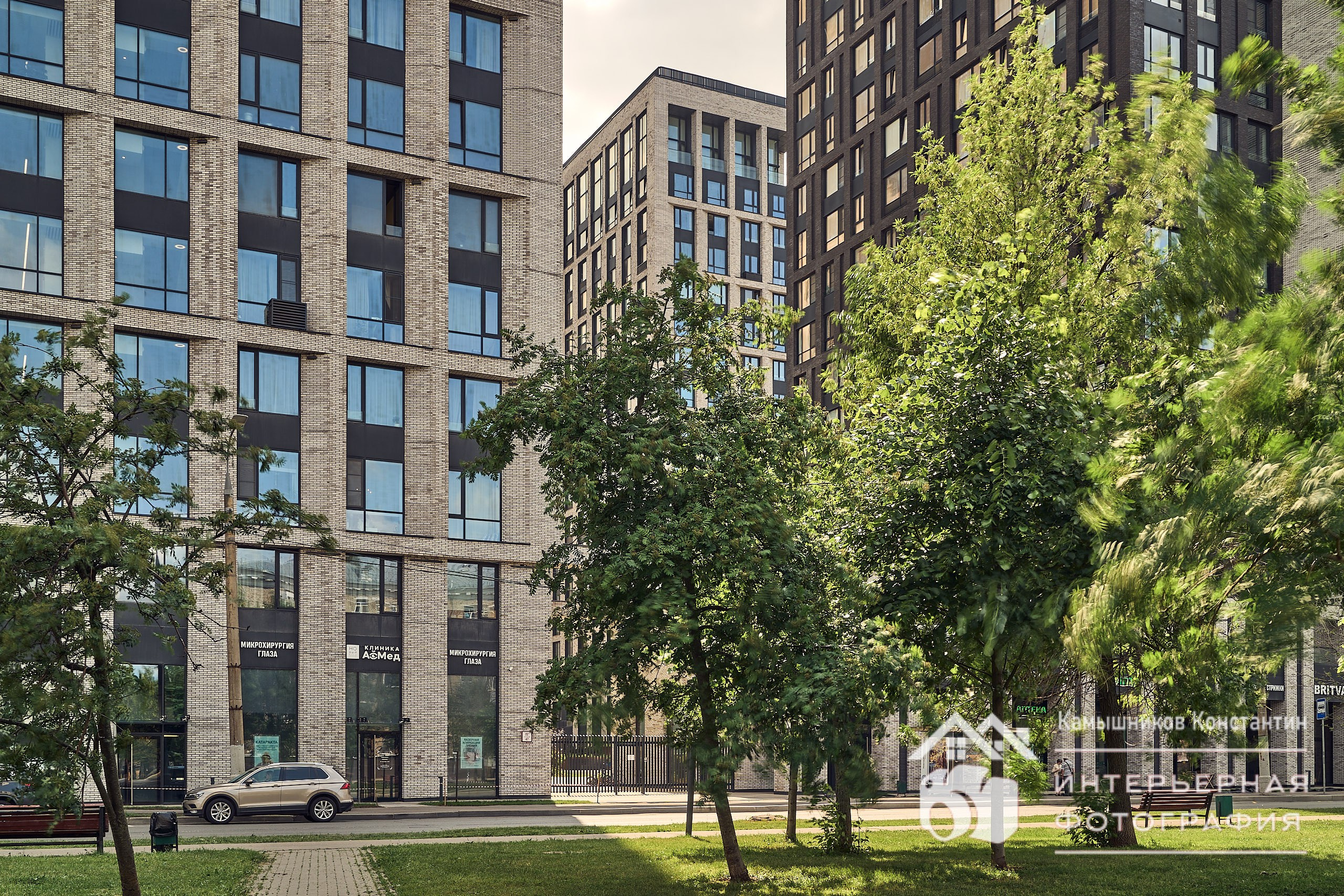 Архитектурное фото нескольких корпусов ЖК бизнес-класса в Москве с идущей перед ними аллей с густой зеленью