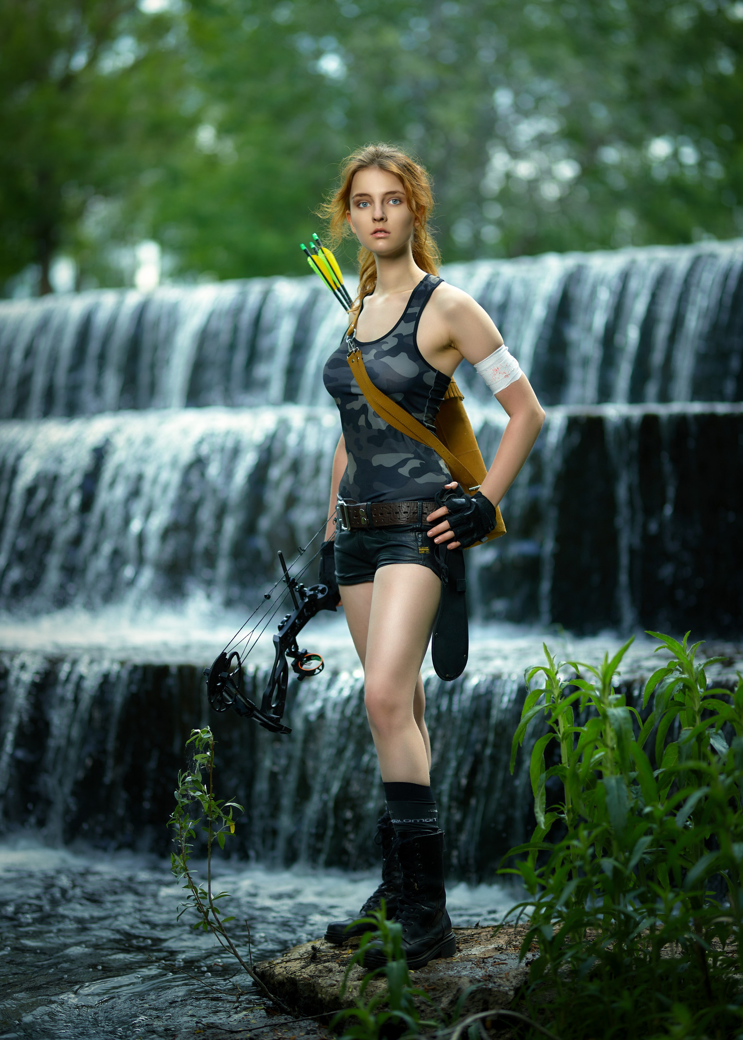 Девочка с луком и стрелами стоит на фоне водопада в торхлово
