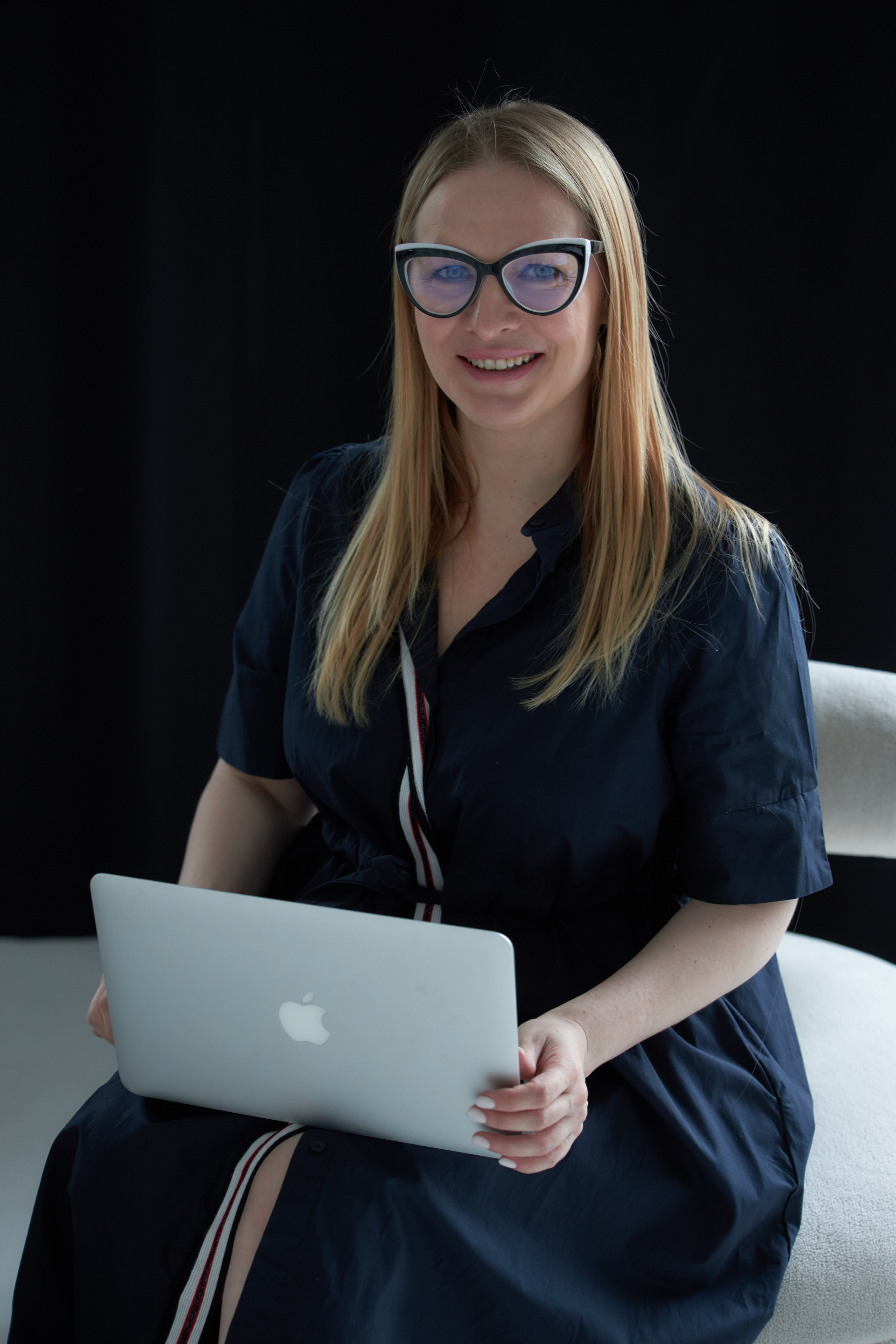 Красивая блондинка в очках сидит с ноутбуком на коленях