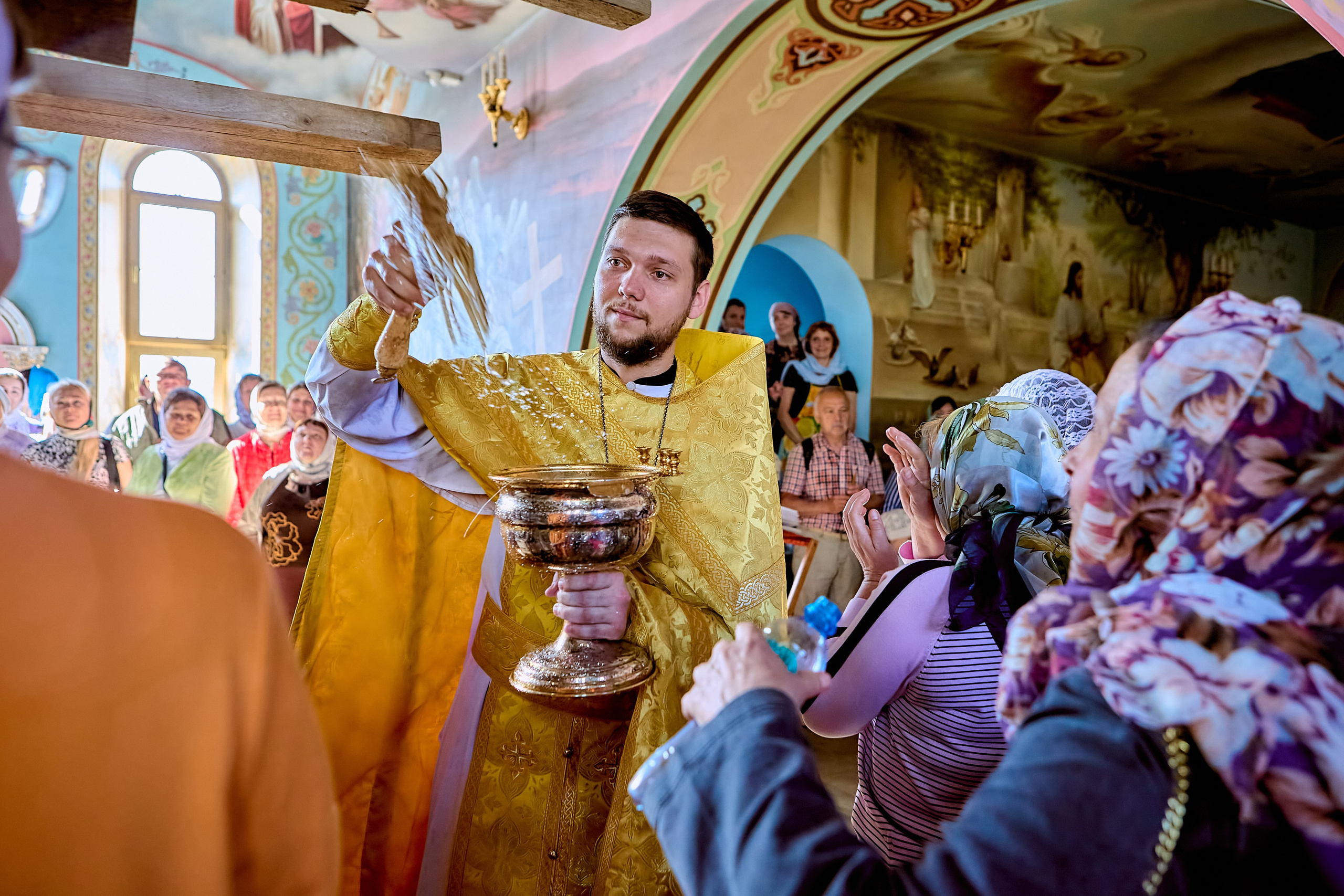 Священник с чашей святой воды окропляет прихожан в храме
