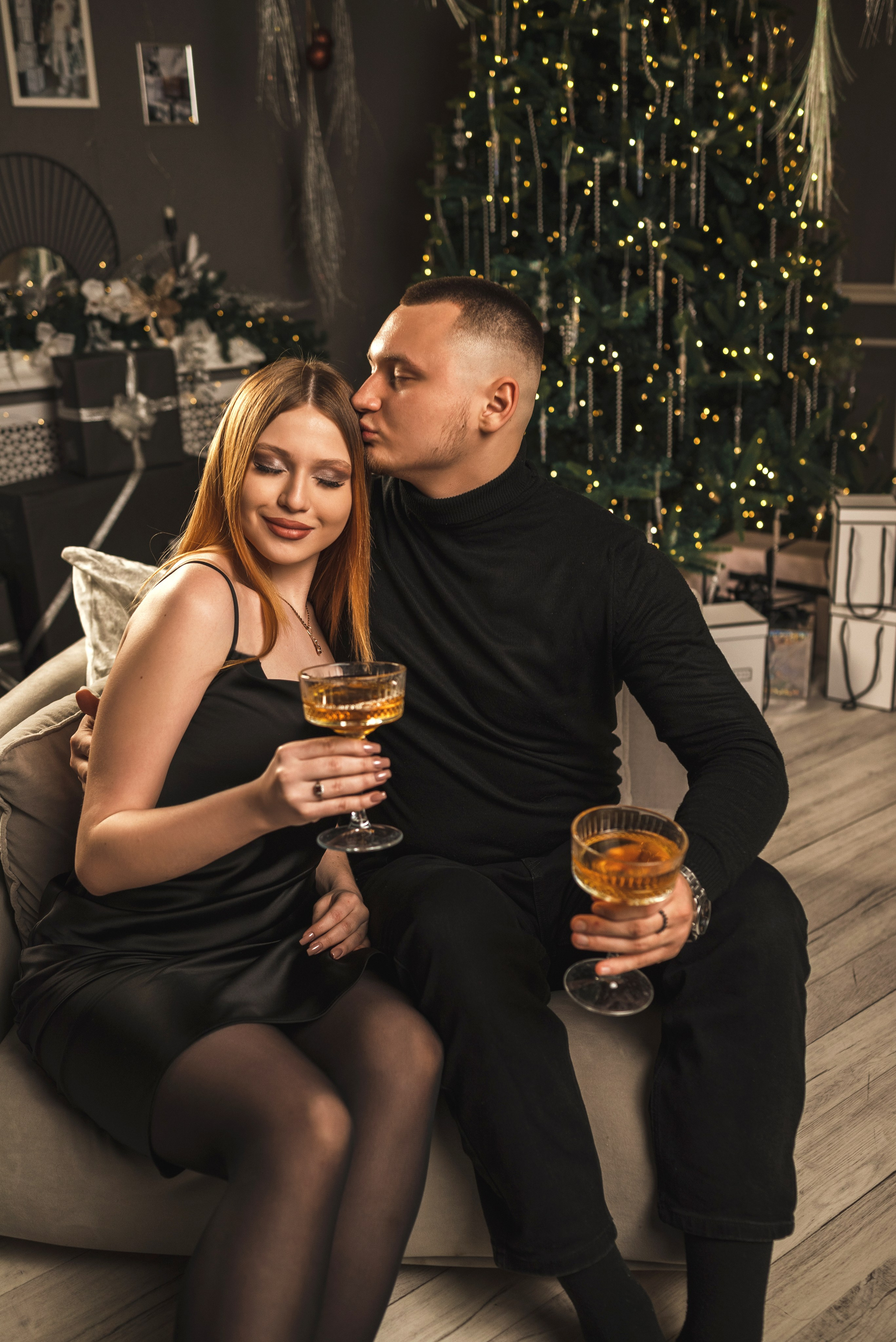 Новогодняя фотосессия 2025 в фотостудии в Каменске-Шахтинском и Ростове-на-Дону. Двое пара молодых сидит с бокалом на фоне новогодней елки. Фотограф Ольга Сагал 