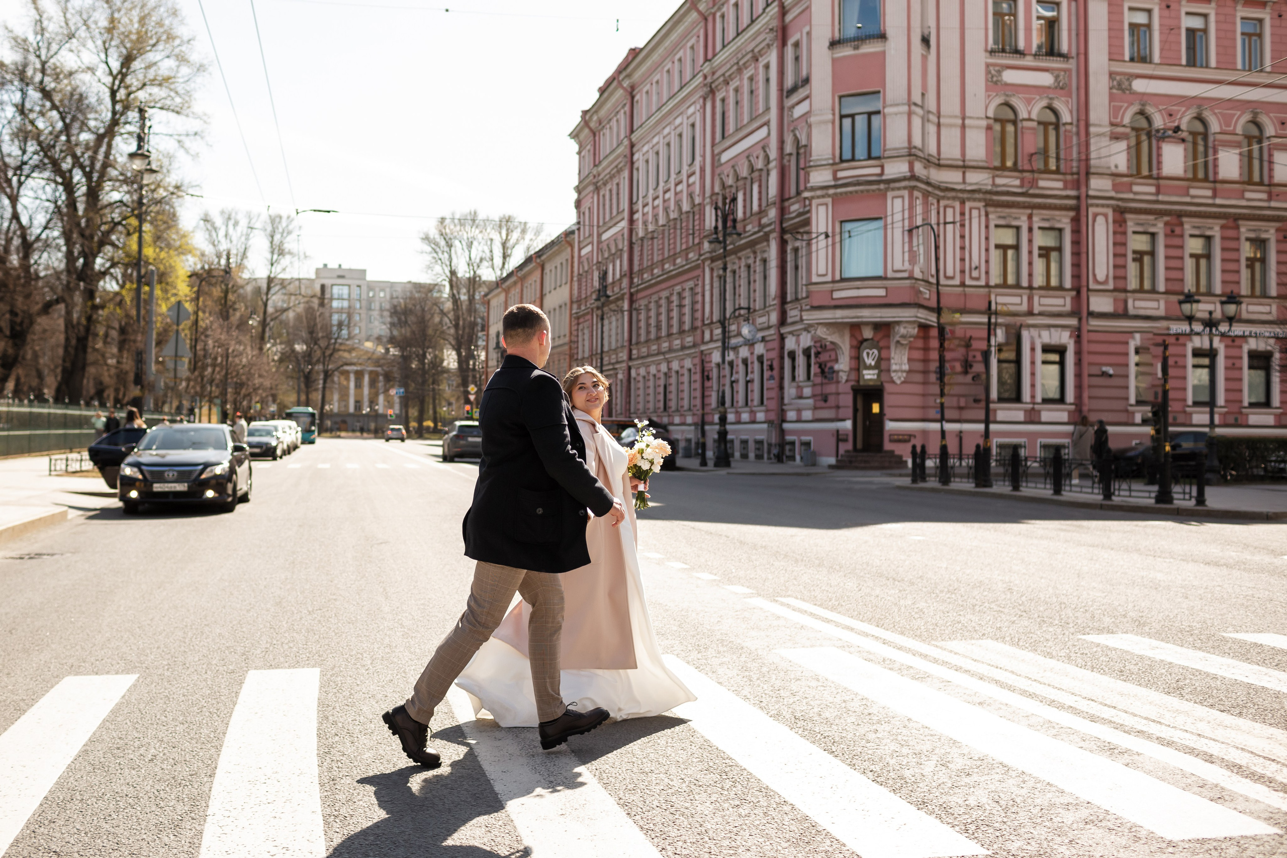 Жених и невеста перебегают улицу в красивых пальто.