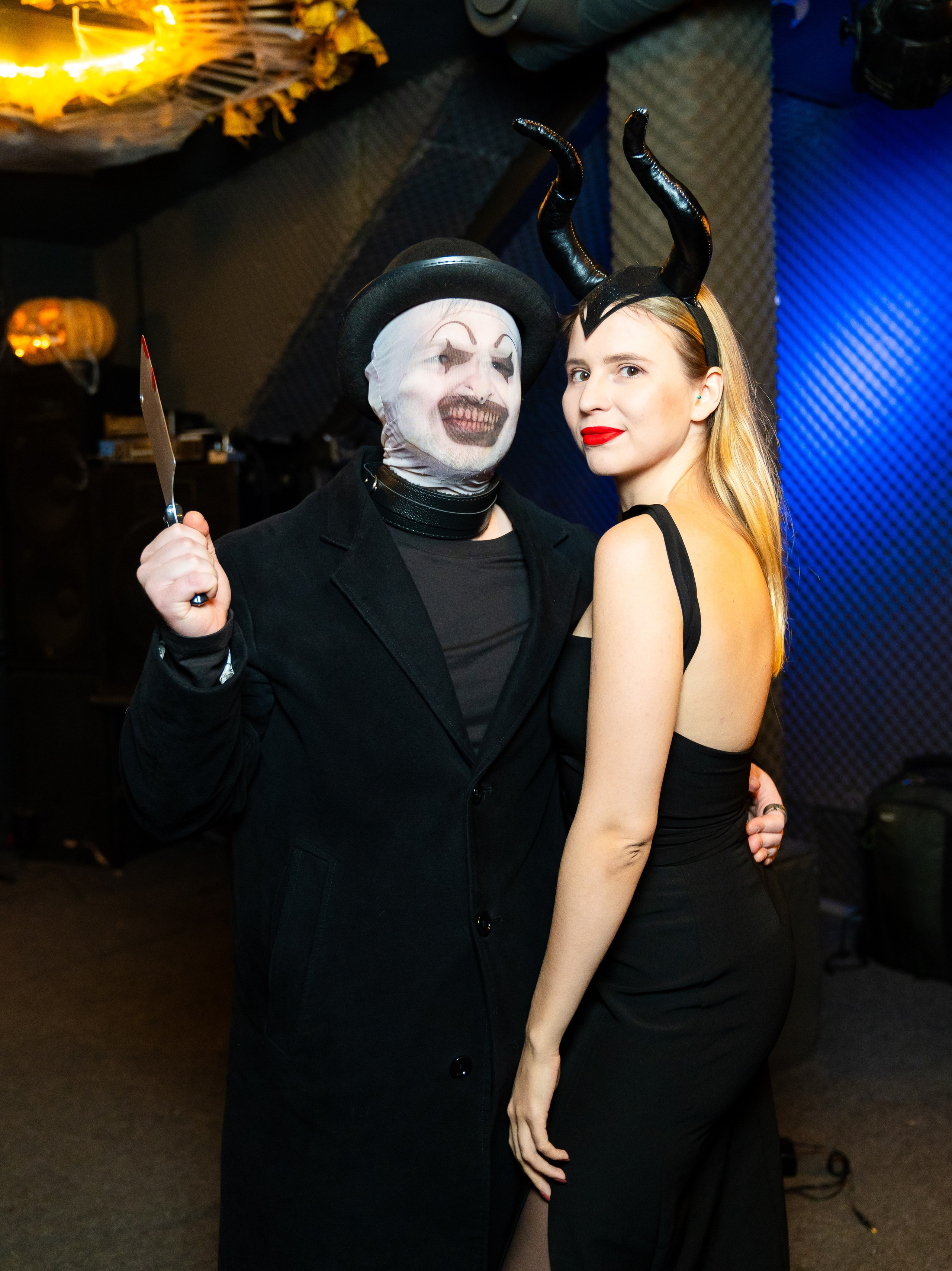 Гости в масках и черных костюмах с реквизитом позируют на фоне Halloween‑декораций бара Debaser, Санкт‑Петербург. Репортажные кадры Хэллоуина 2025, эмоции и костюмы, фото Евгения Мальцева.