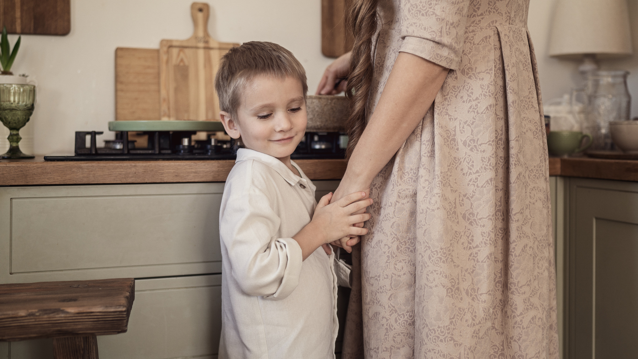 Мальчик держит маму за руку пока она что-то готовит на плите