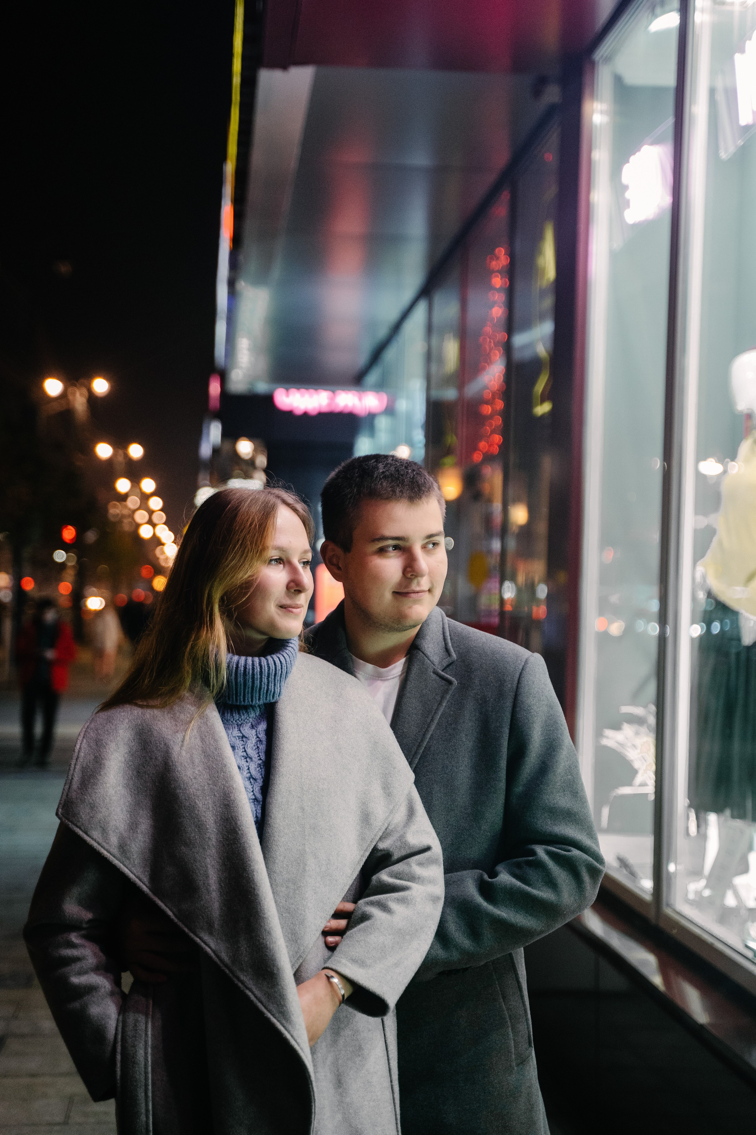 парень с девушкой в пальто весной позируют на фоне витрины 