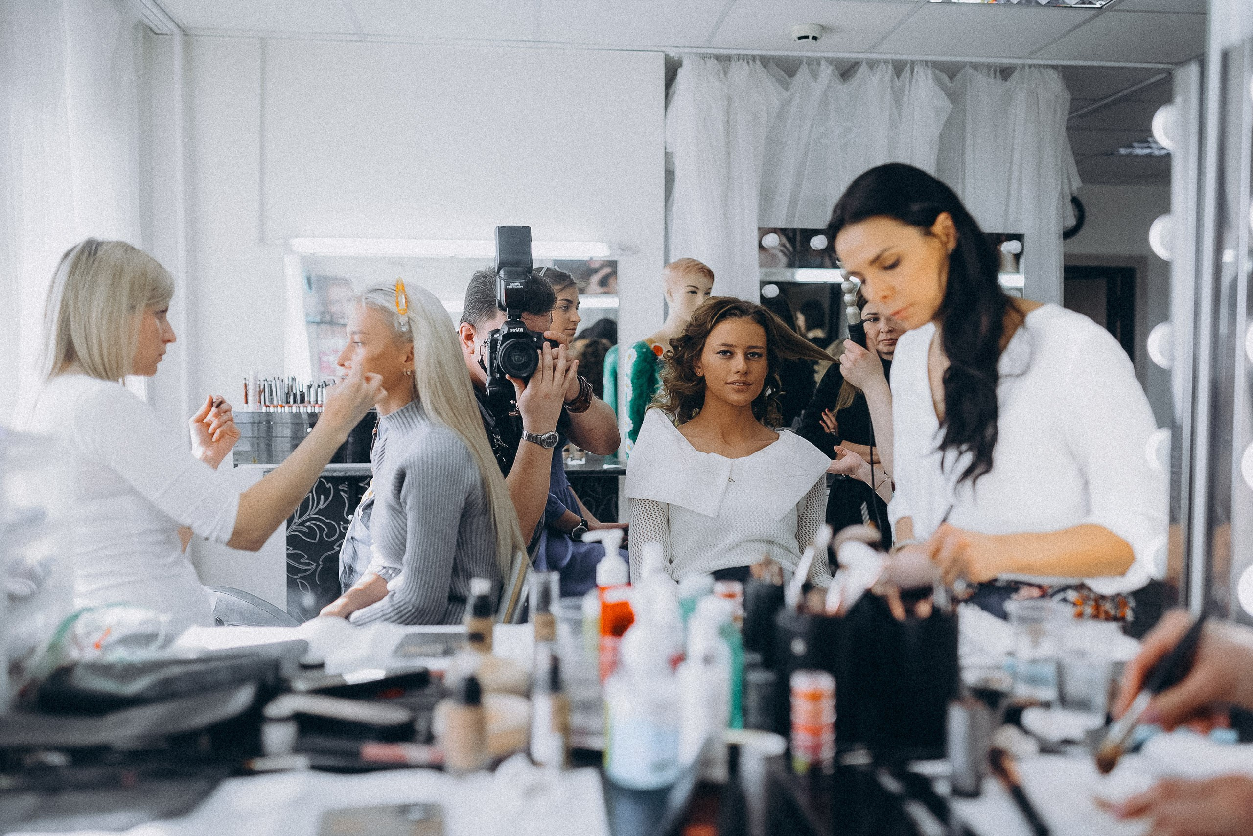 Общий план гримерной: суета и атмосфера закулисья профессионального конкурса красоты.