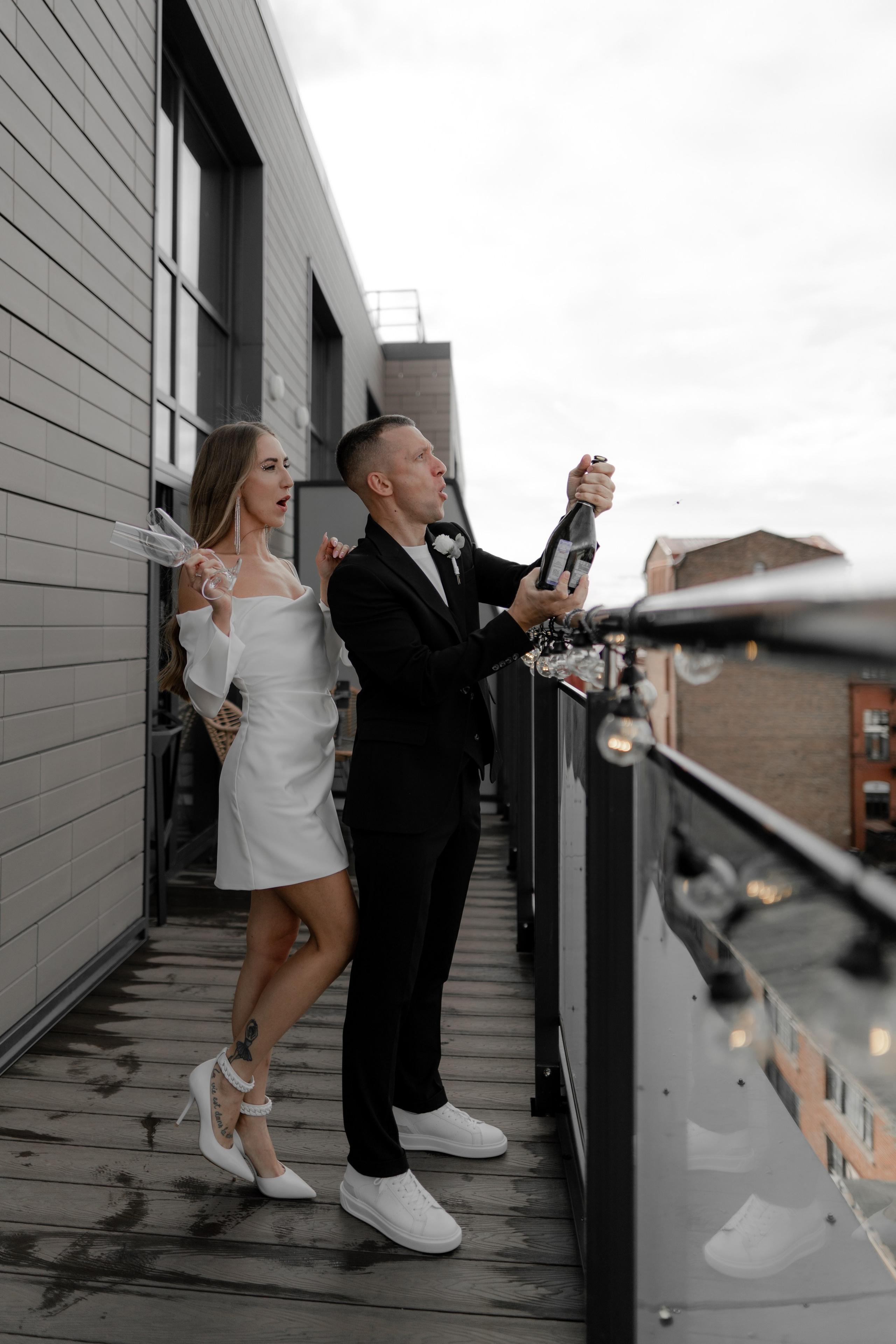 Жених и невеста стоят на балконе и открывают шампанское