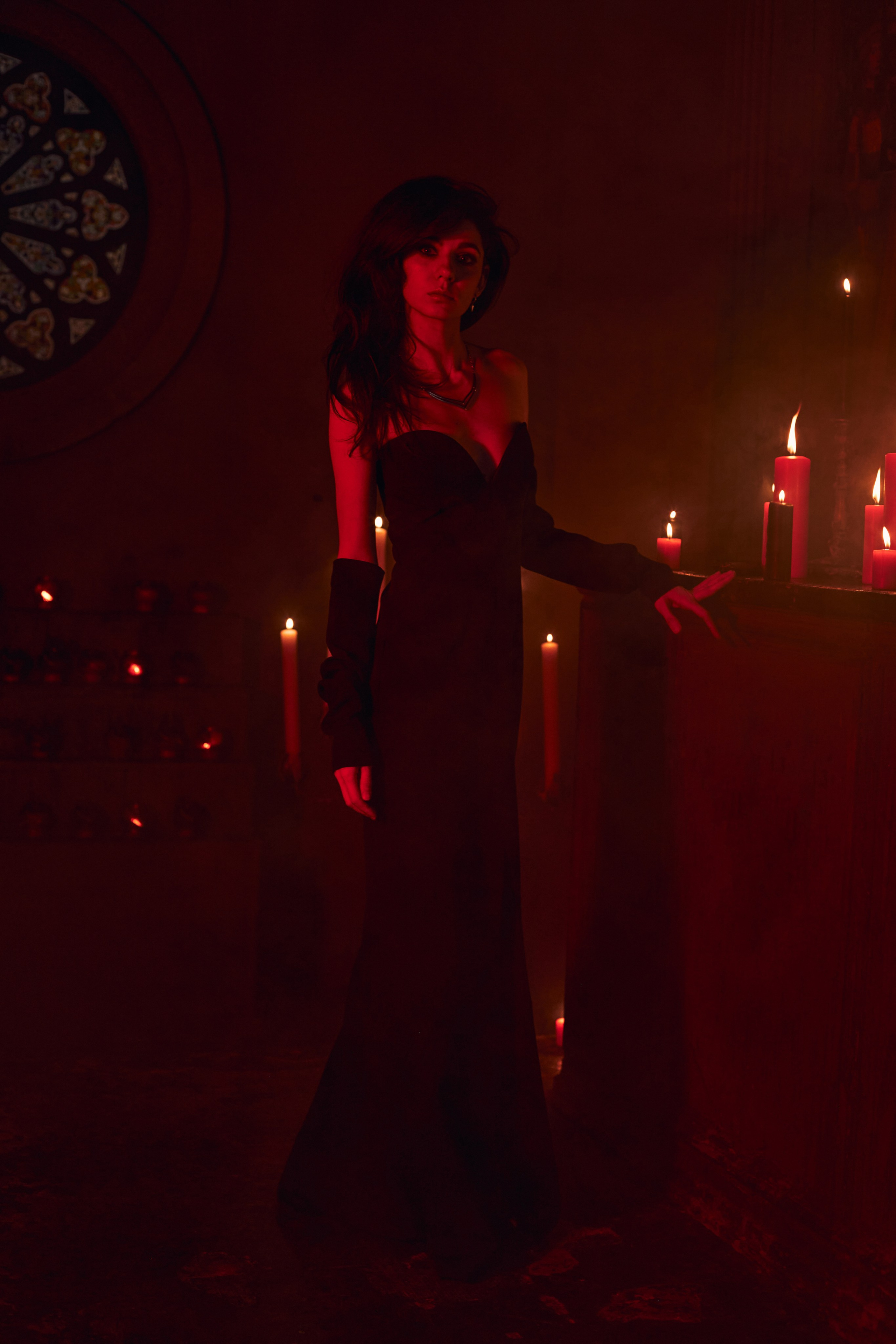 Портрет красивой темноволосой девушки, стоящей у алтаря с горящими свечами в полный рост